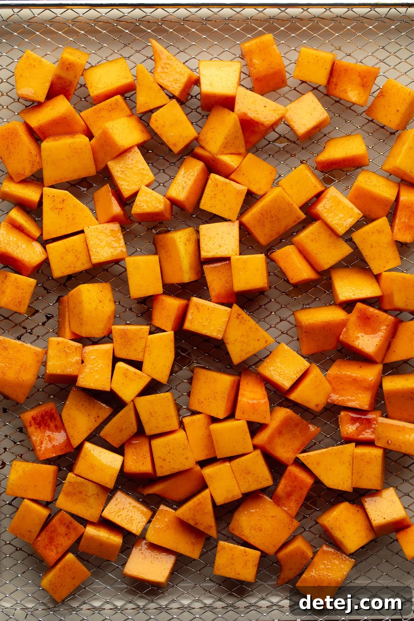 overhead view of spiced butternut squash cubes in an even layer in an air fryer basket.