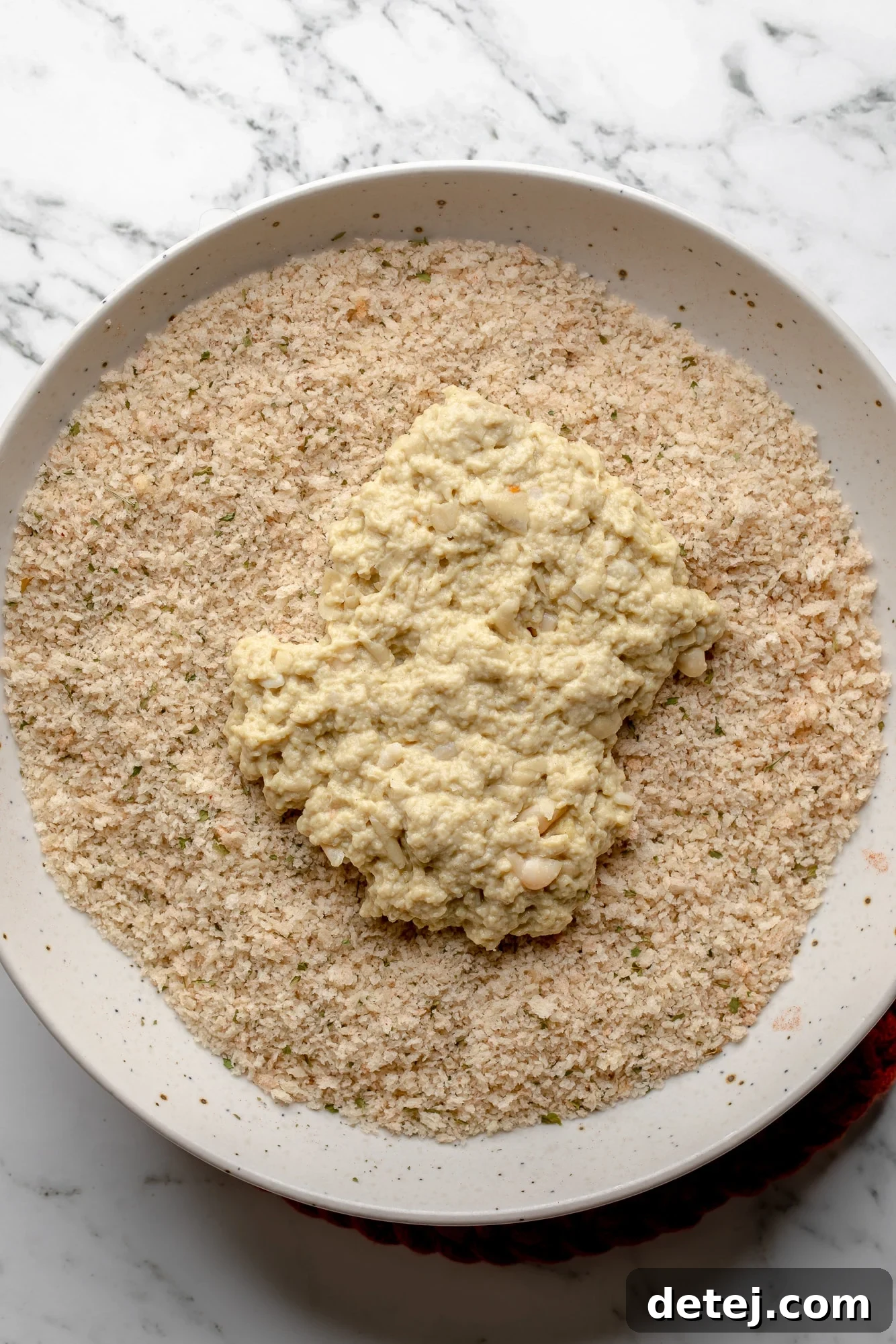 Coating a piece of seitan in breadcrumbs in a white bowl, demonstrating the breading process.