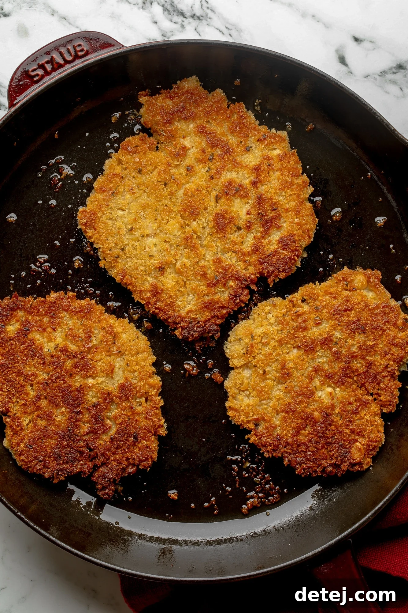 Overhead view of crispy golden breaded vegan cutlets frying in a large black skillet, showcasing the cooking process.
