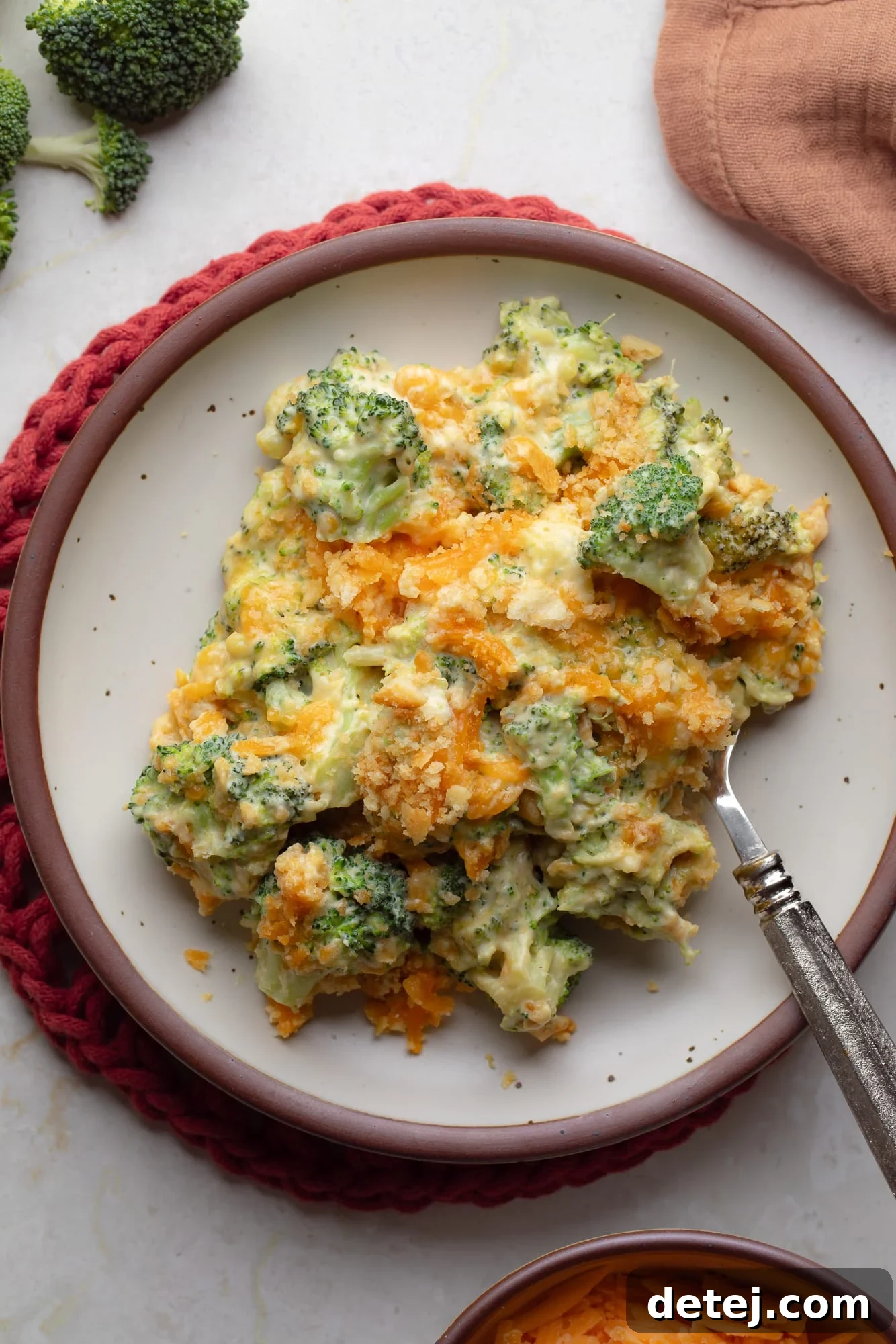 An overhead shot revealing a perfectly portioned scoop of vegan broccoli casserole on a plate, highlighting its creamy texture, vibrant green broccoli, and golden cracker topping.