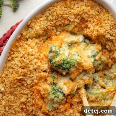 A spoon lifting a scoop of creamy, cheesy vegan broccoli casserole from a large baking dish, ready to be savored.