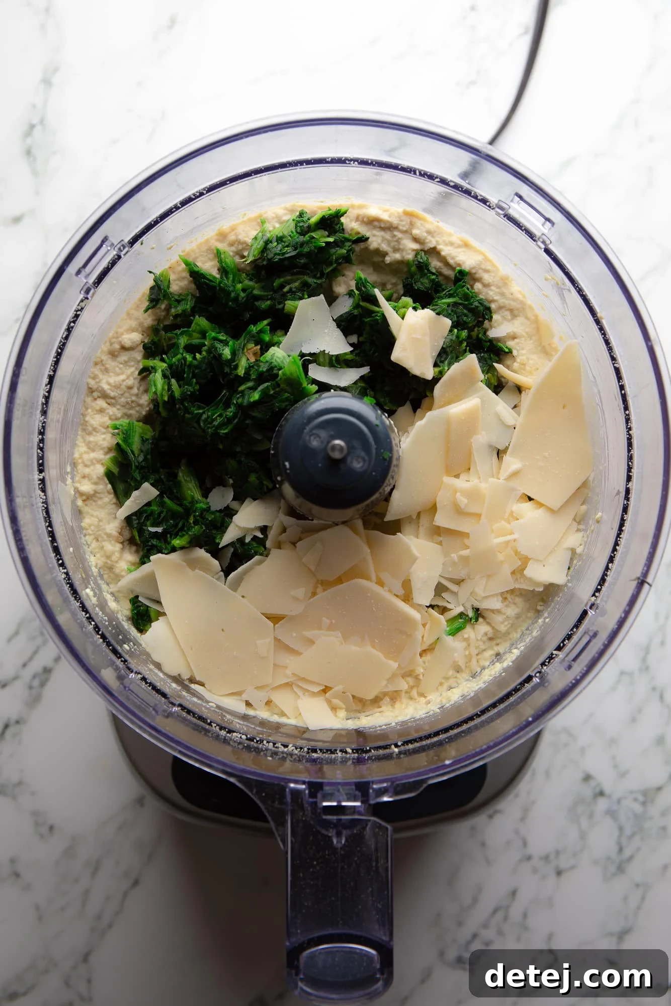Overhead view of various vegan ricotta cheese ingredients, including cashews, tofu, and nutritional yeast, prepared in a food processor.