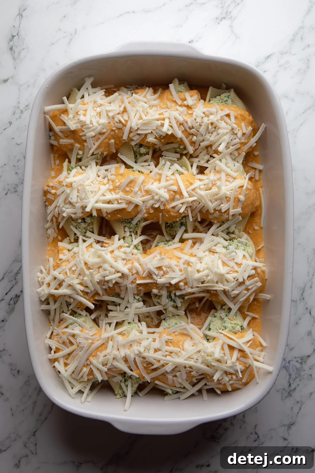 Overhead shot of vegan pumpkin stuffed shells covered in rich pumpkin sauce and shredded vegan cheese, ready to be baked in a casserole dish.