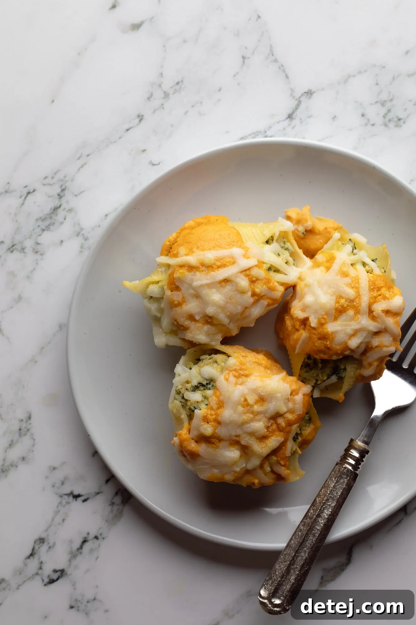 Overhead view of three individual vegan pumpkin stuffed shells, perfectly baked and garnished, served on a rustic plate.