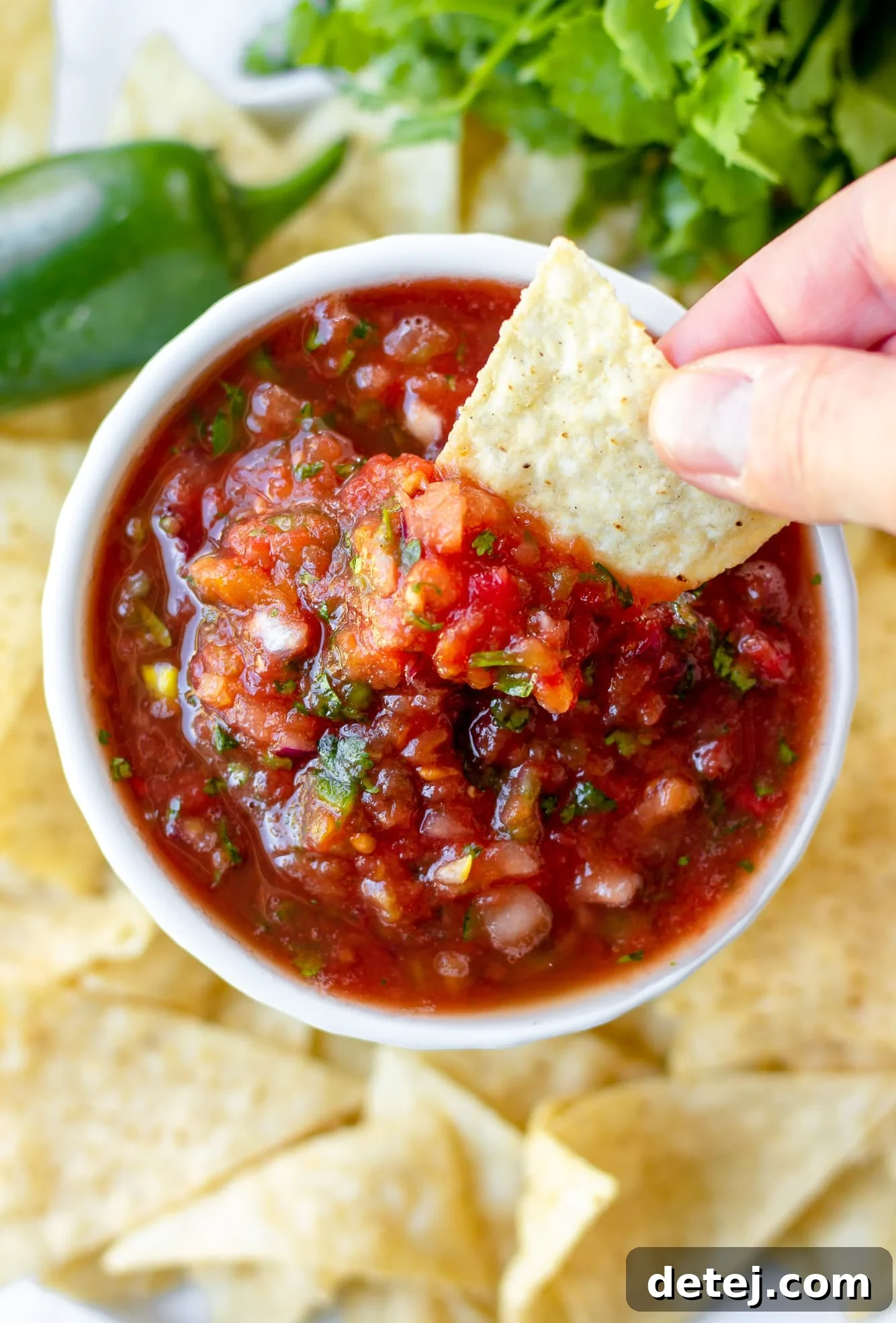 Effortless Fresh Salsa 2 Woman's hand dipping a tortilla chip into a small bowl of vibrant homemade tomato salsa, showcasing its irresistible texture.