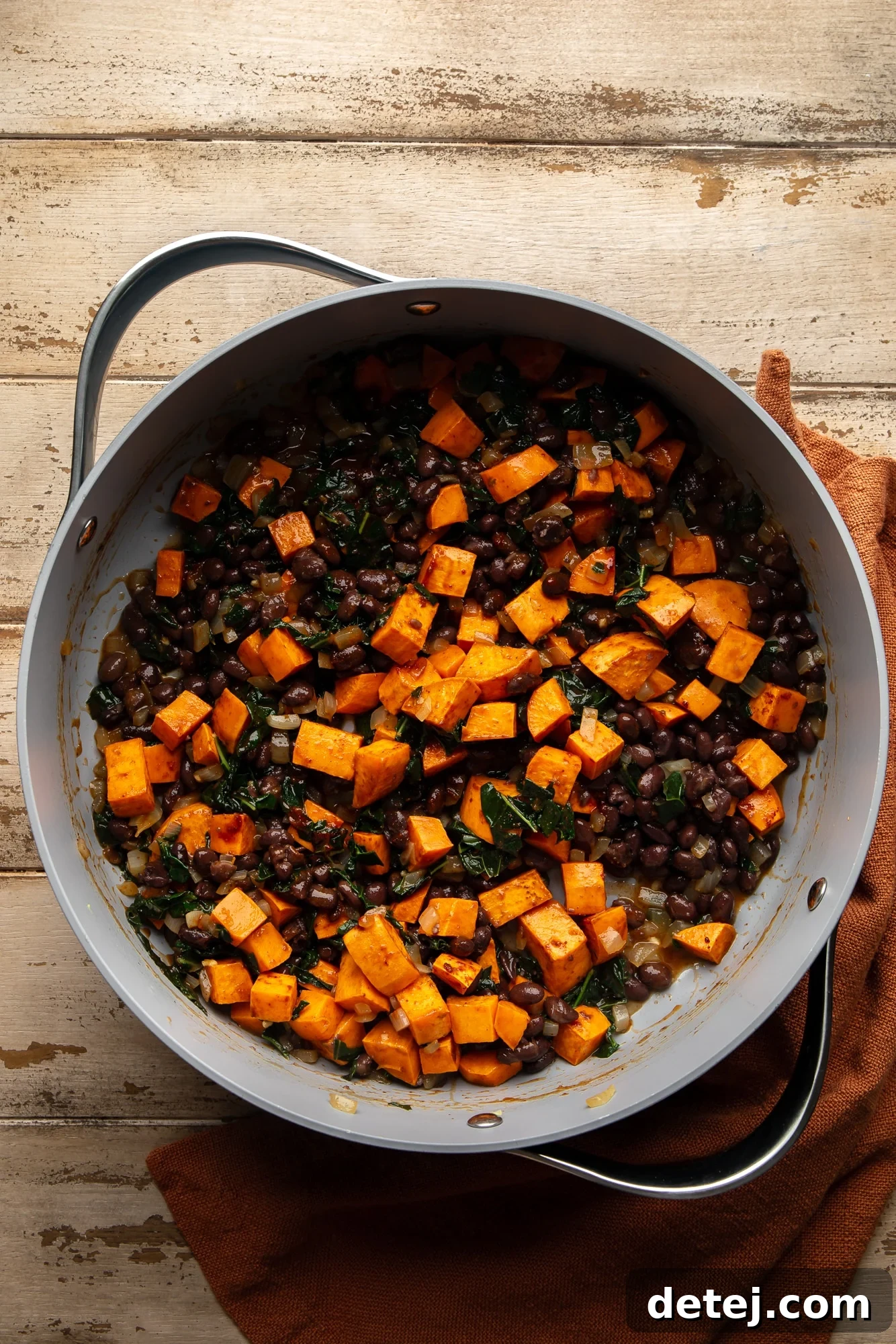 cooking sweet potatoes and black beans with kale and spices in a large pot, showing the vibrant ingredients mixing together.