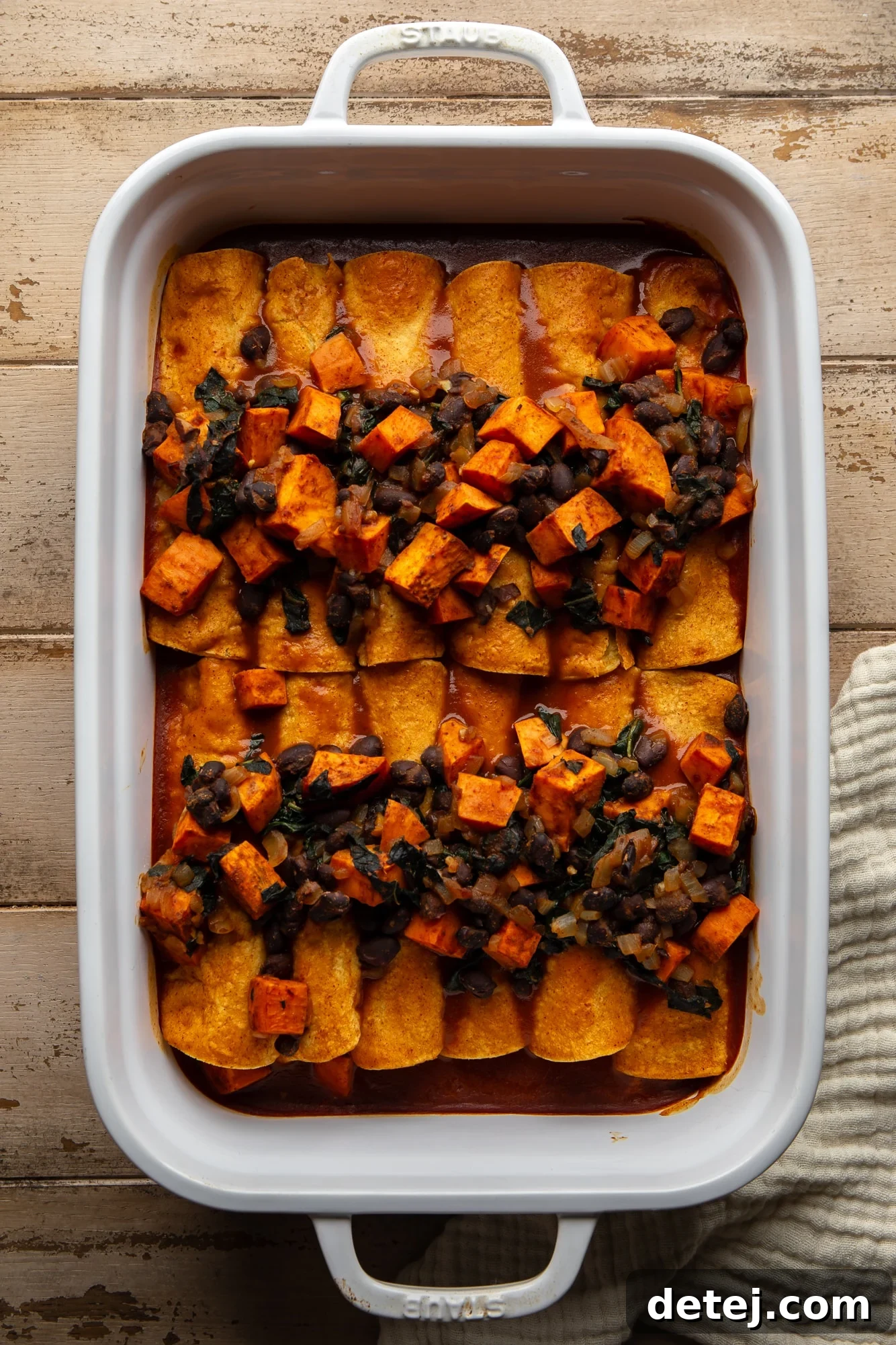 assembled sweet potato black bean enchiladas neatly arranged in a large casserole dish, ready for baking.