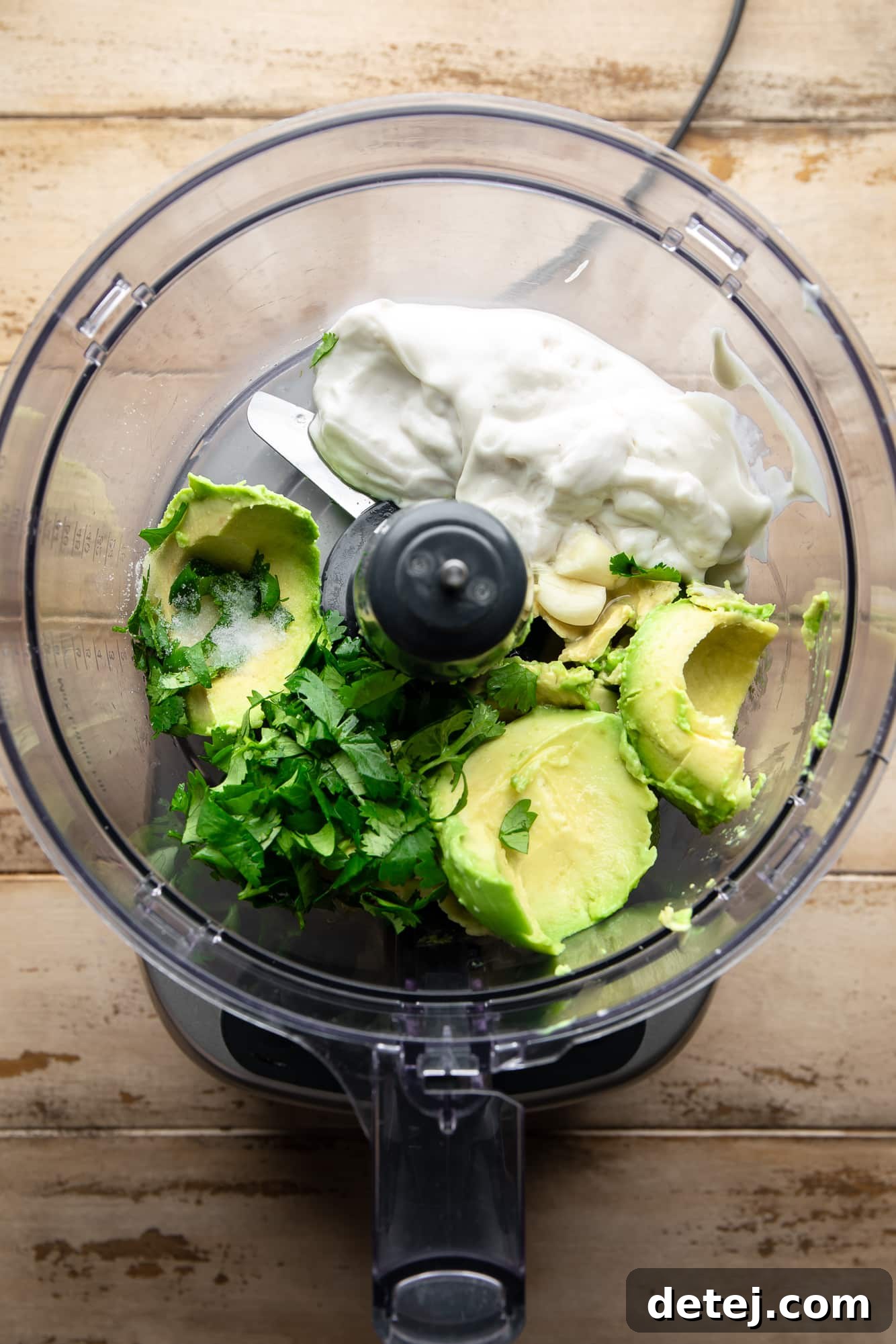 the ingredients for vegan avocado crema, including avocado, yogurt, lime, and cilantro, placed in a food processor before blending.