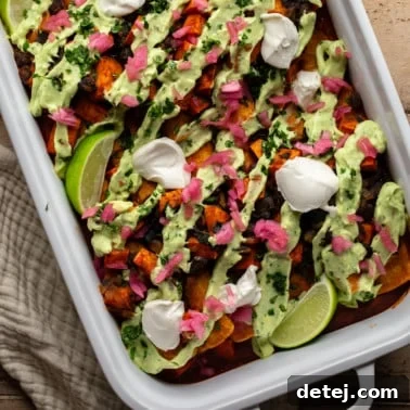 overhead view of sweet potato black bean enchiladas topped with avocado crema, vegan sour cream, pickled red onions, and lime wedges.