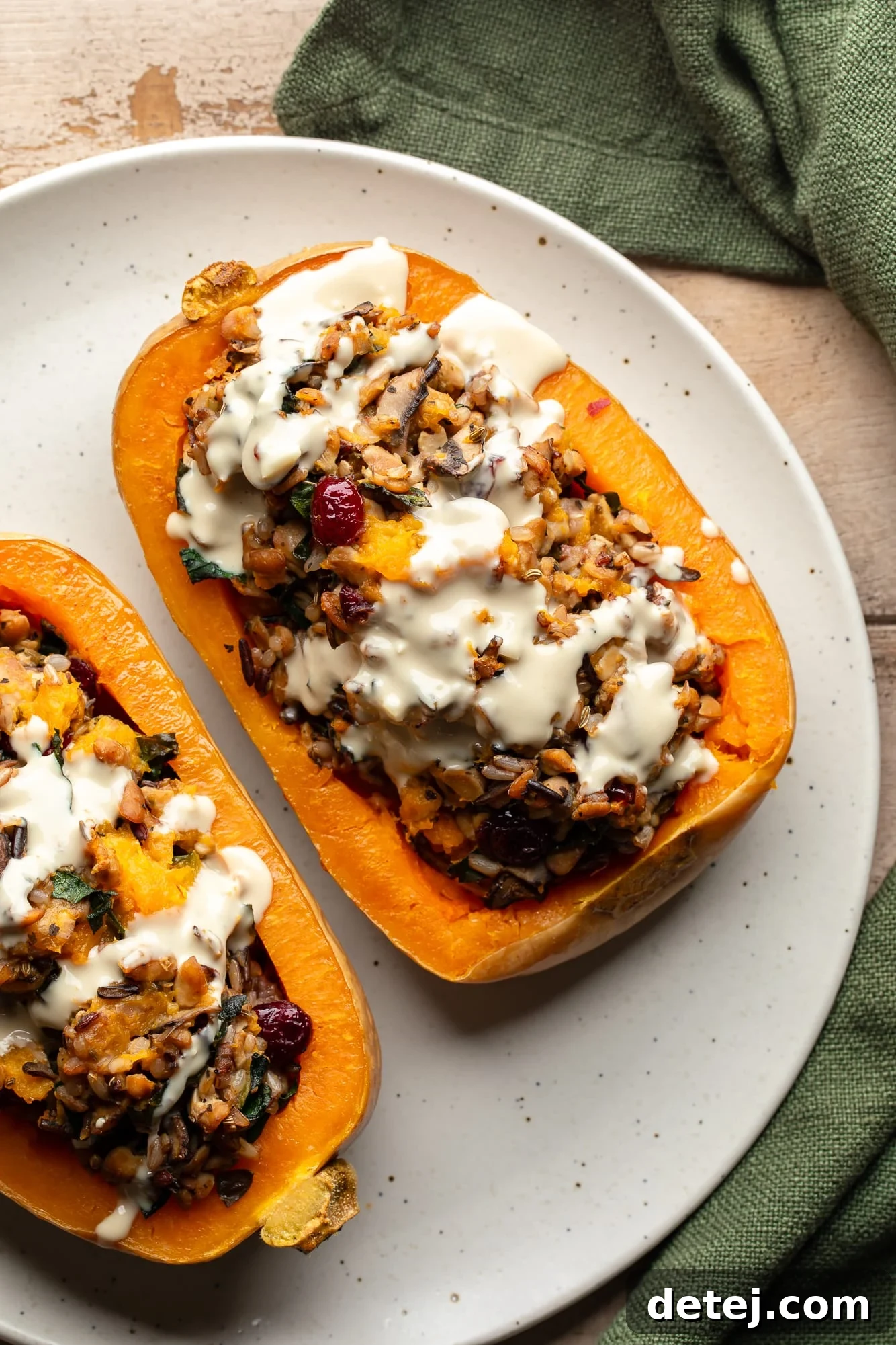 overhead view of two stuffed butternut squashes topped with garlic tahini sauce on a white plate, showcasing a rich, savory filling.