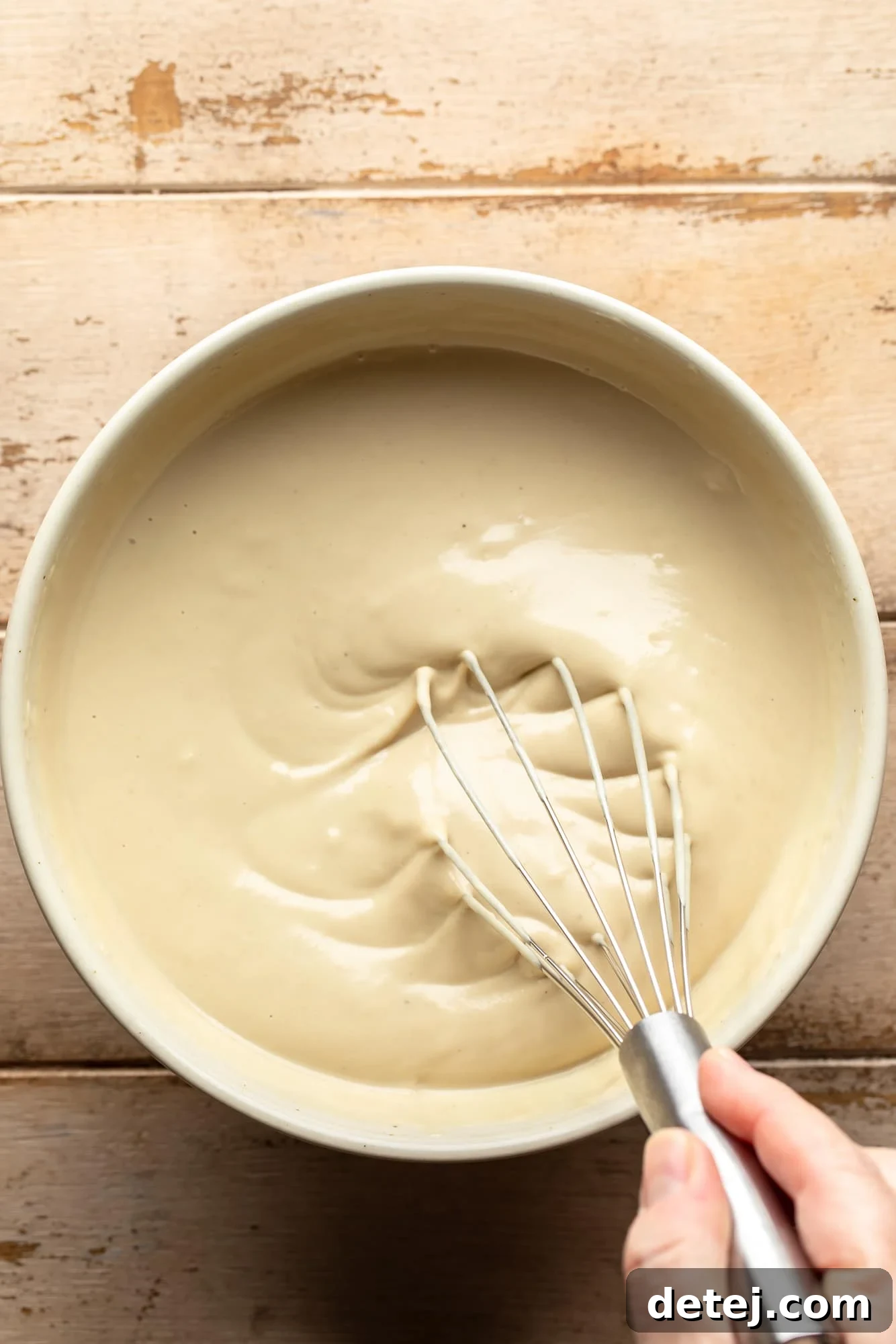 a woman's hand expertly whisking garlic tahini sauce in a large white bowl, creating a smooth and creamy texture.