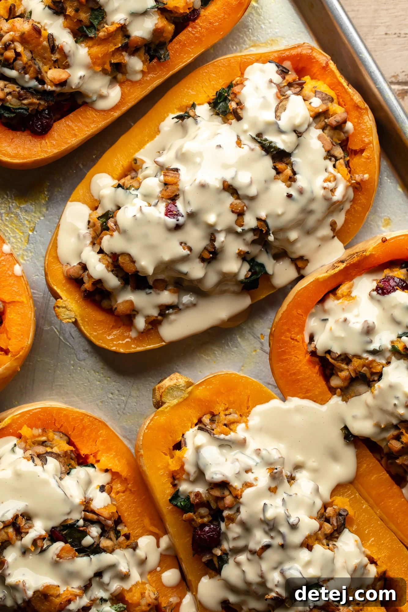 overhead view of stuffed butternut squashes generously topped with garlic tahini sauce on a baking dish, ready to be served.