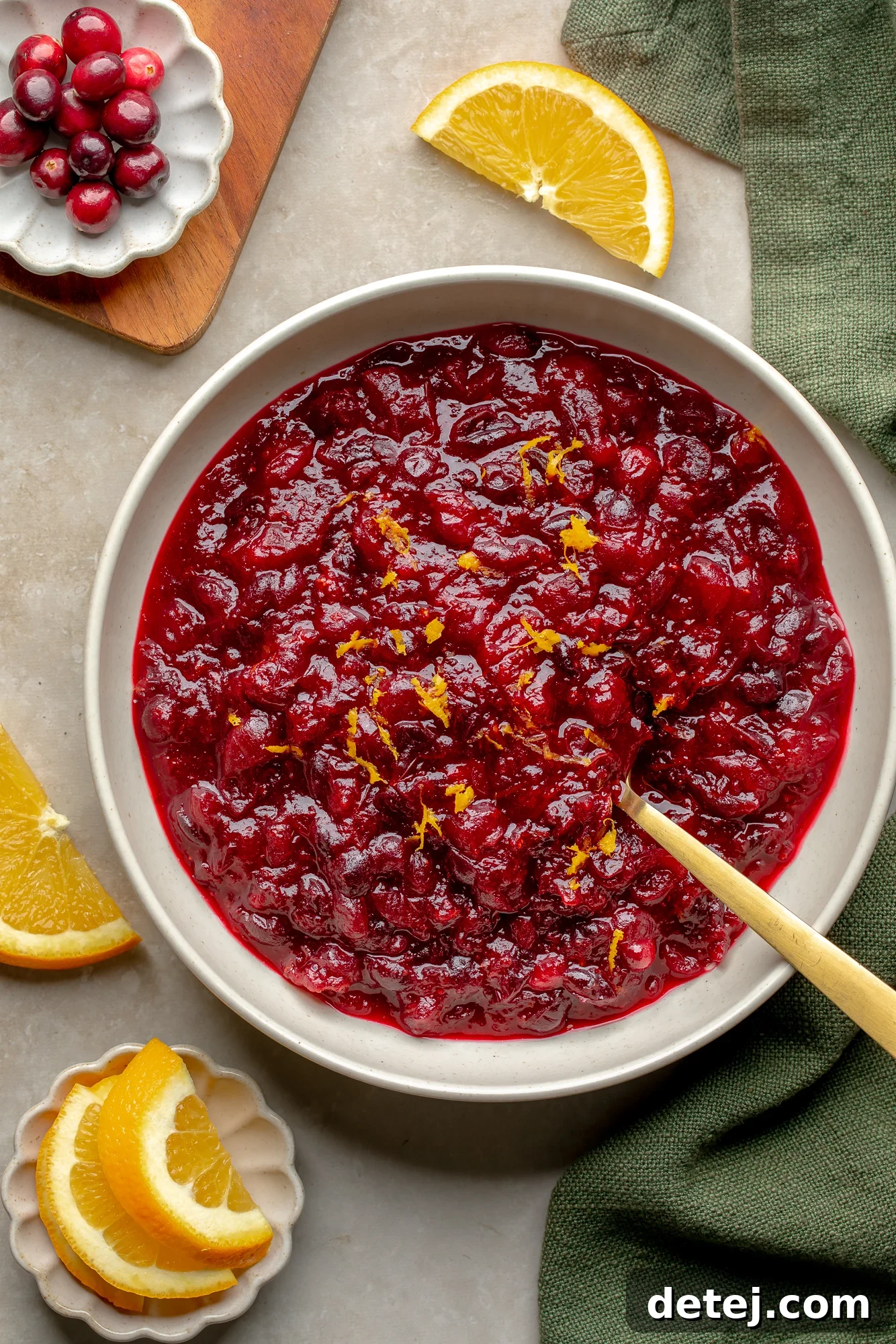 Ruby Orange Cranberry Delight 2 Overhead view of a bowl of orange cranberry sauce topped with orange zest with orange slices and fresh cranberries on the side.