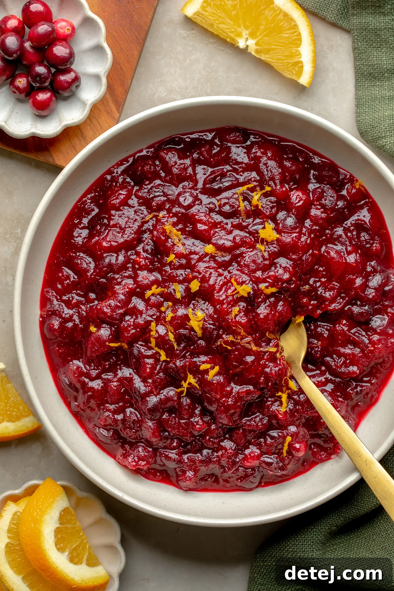 Ruby Orange Cranberry Delight 7 Overhead view of a bowl of orange cranberry sauce topped with orange zest with orange slices and fresh cranberries on the side.