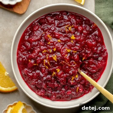 Ruby Orange Cranberry Delight 8 Overhead view of a bowl of orange cranberry sauce topped with orange zest with orange slices and fresh cranberries on the side.