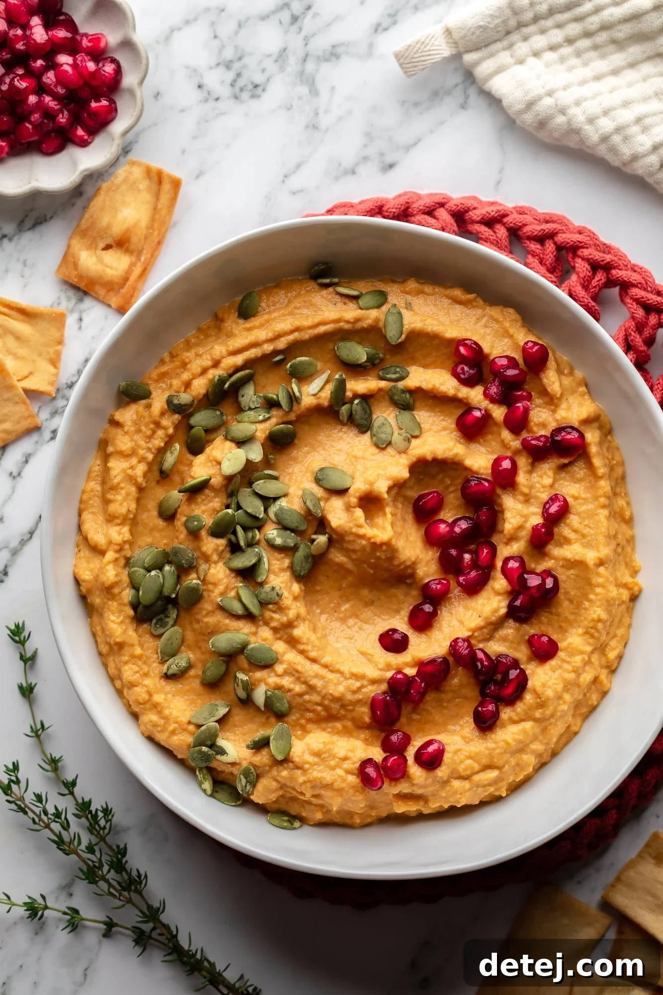 overhead view of a bowl of orange pumpkin hummus topped with pumpkin seeds and pomegranate seeds.