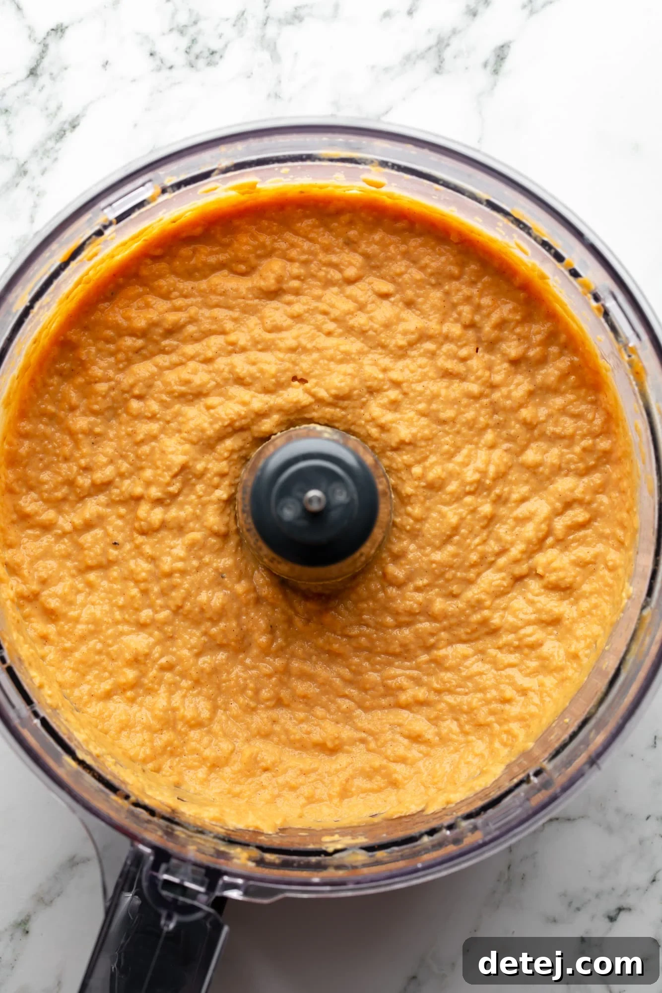 overhead view of a bowl of orange pumpkin hummus in a food processor.