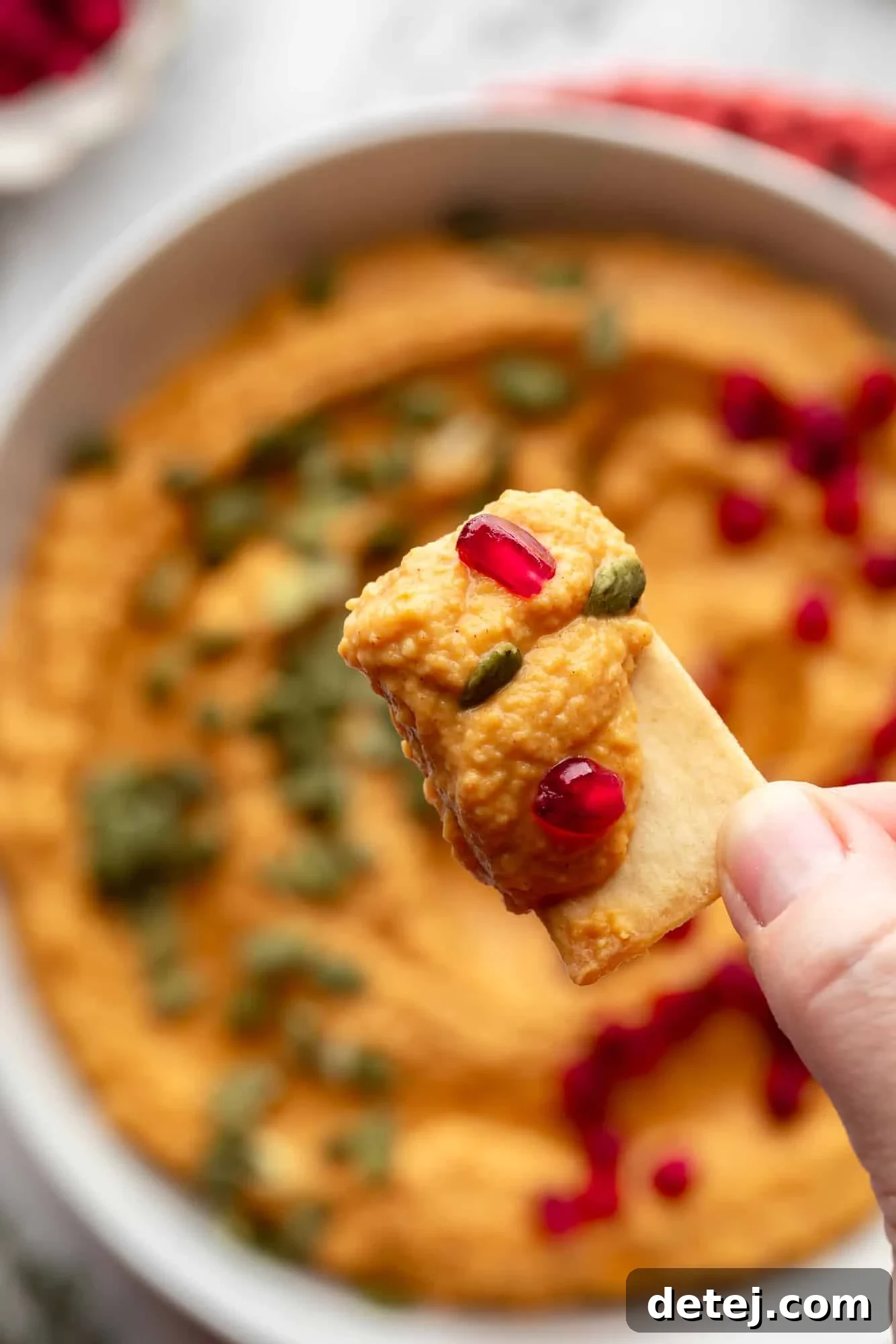 close up on a womans hand holding a pita chip covered in pumpkin hummus.