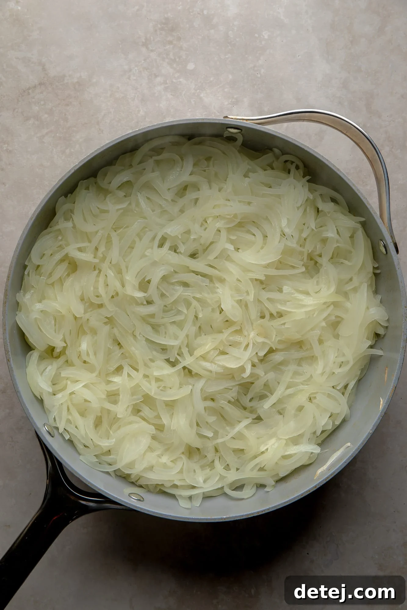 Close-up overhead view of thinly sliced onions gently cooking and beginning to soften in a large skillet.