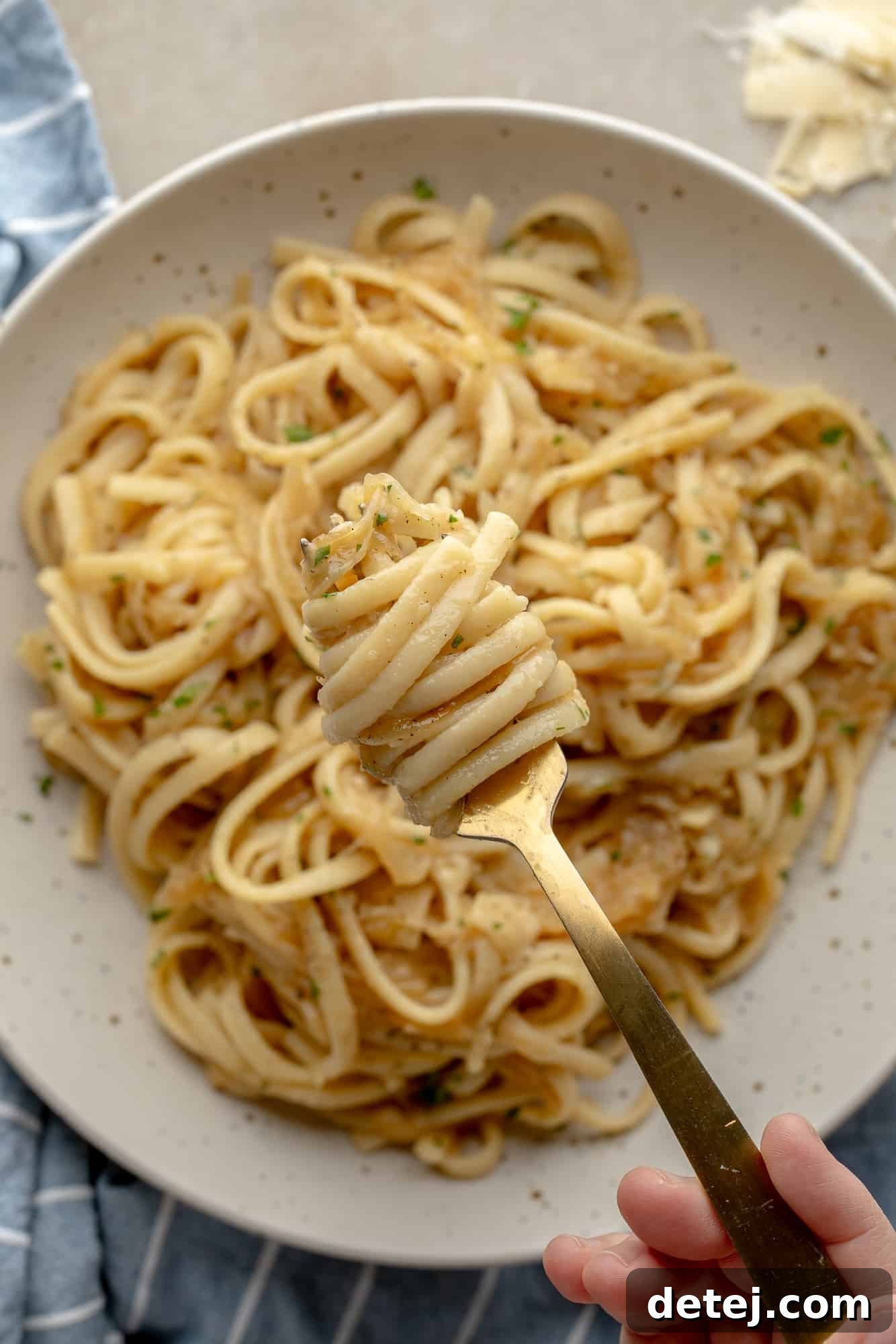 Close-up view of a fork lifting a perfect bite of vegan caramelized onion pasta, showcasing the creamy sauce and tender onions, above a full bowl.