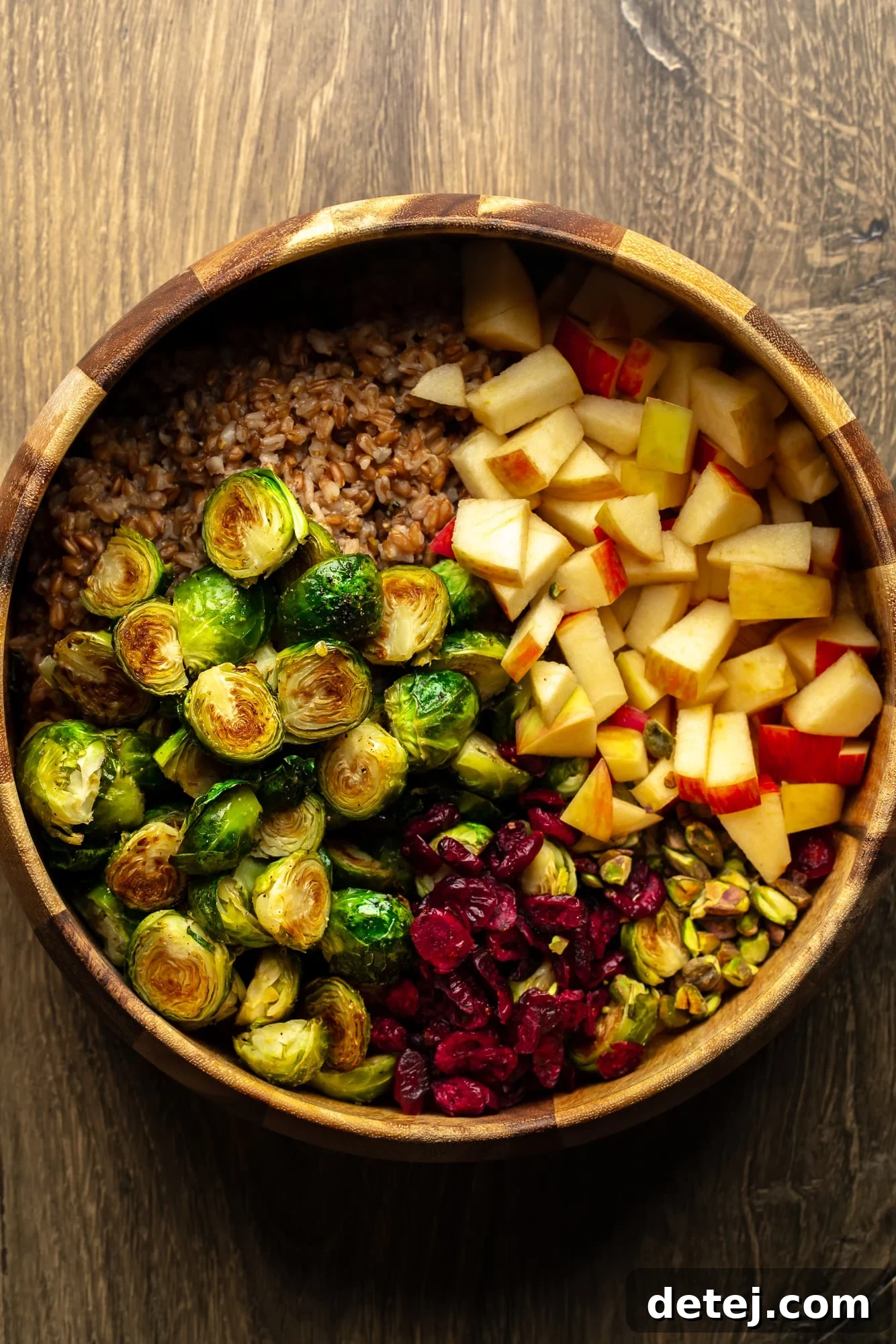 Various fresh ingredients for warm brussels sprouts salad, including farro, cranberries, nuts, and chopped apples, laid out in a large bamboo bowl, showcasing the readiness for assembly.