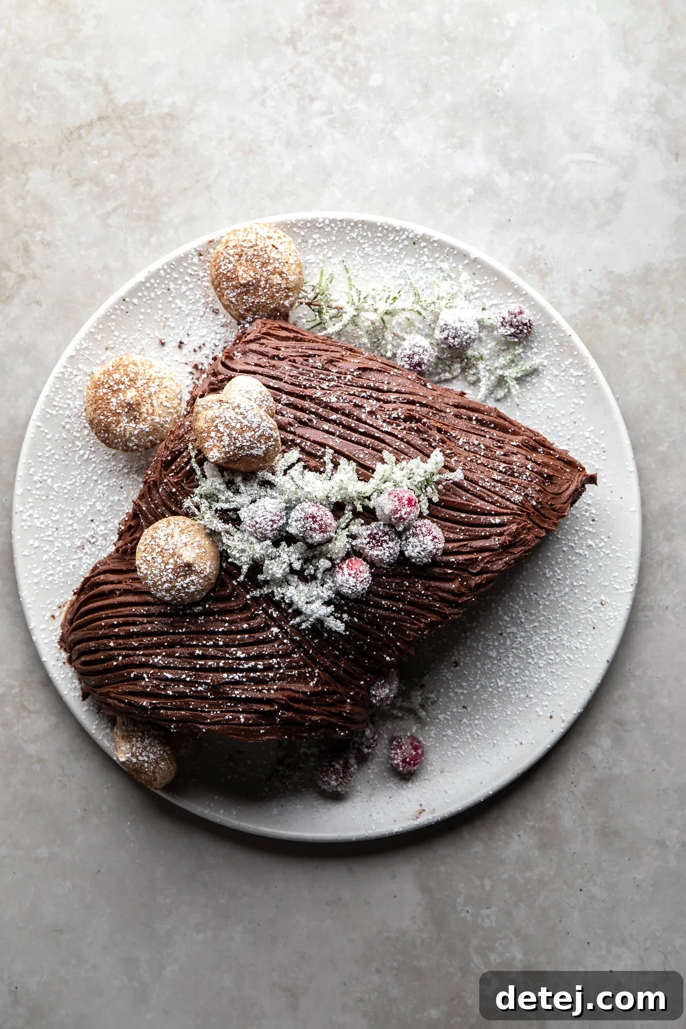 overhead view of a vegan yule log cake topped with sugared cranberries and meringue mushrooms on a white plate.