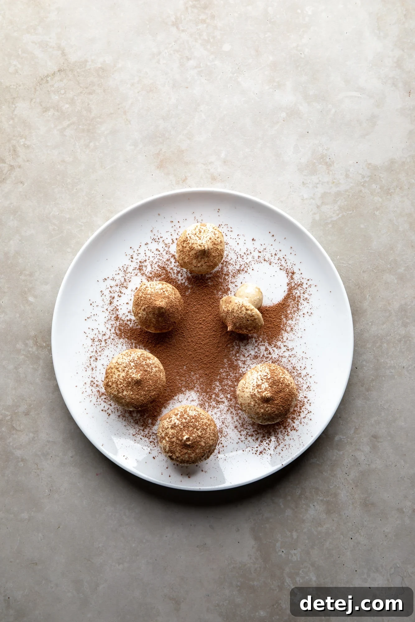 overhead view of vegan meringue mushrooms dusted with cocoa powder on a white plate.