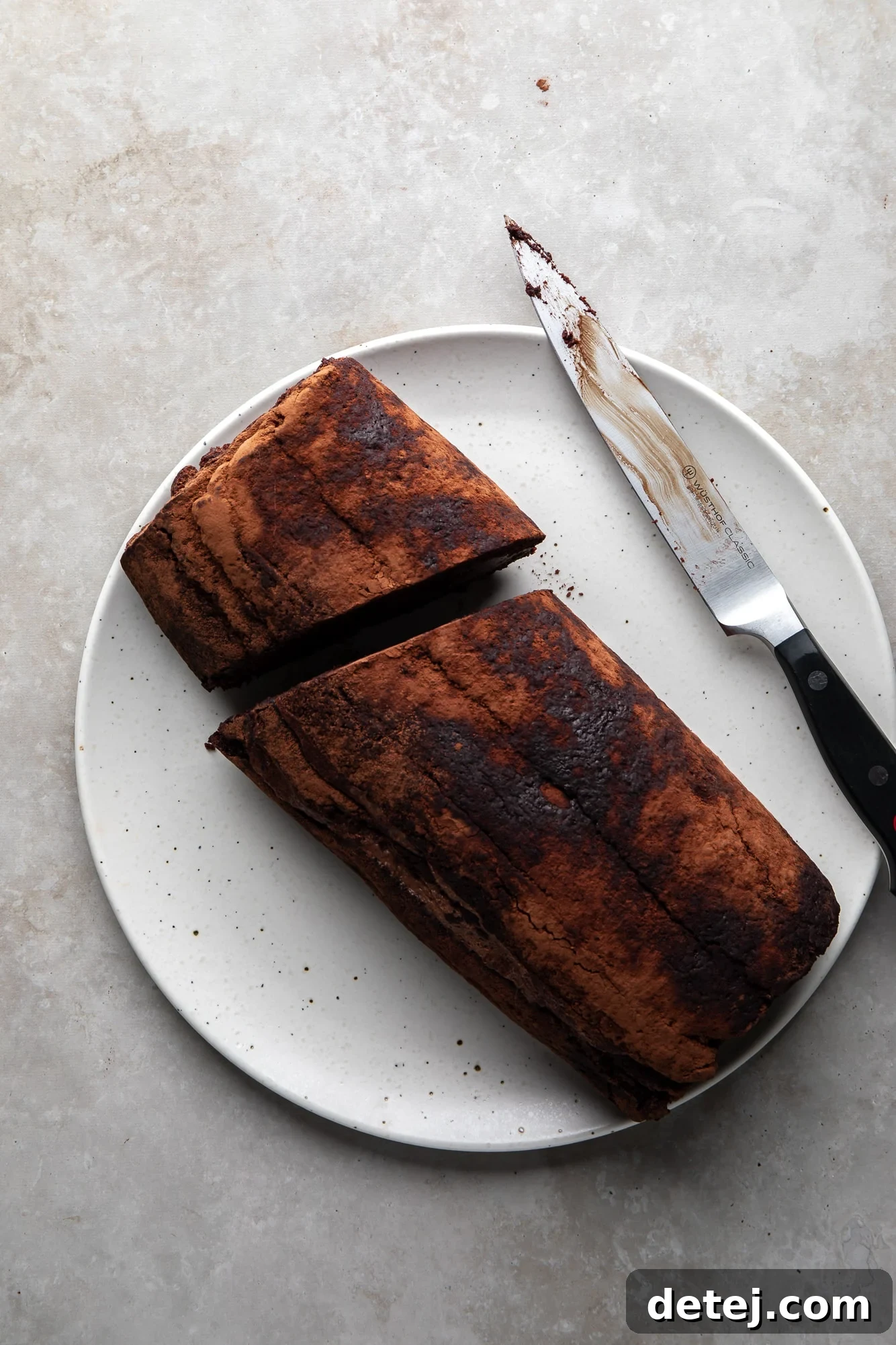overhead view of a rolled yule log sliced in half next to a knife on a white plate.