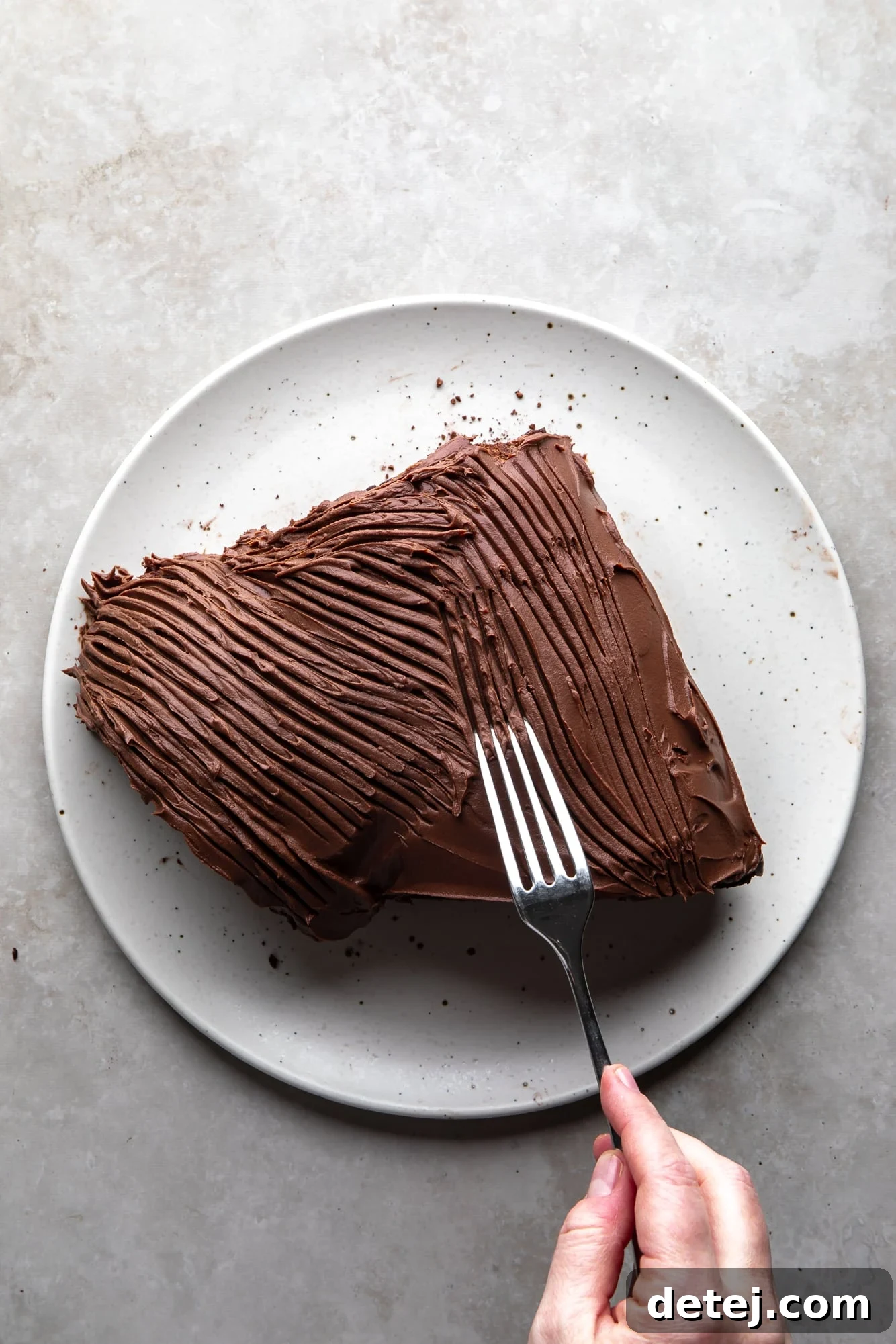 overhead view of a womans hand dragging a fork over a frosted yule log cake on a white plate.