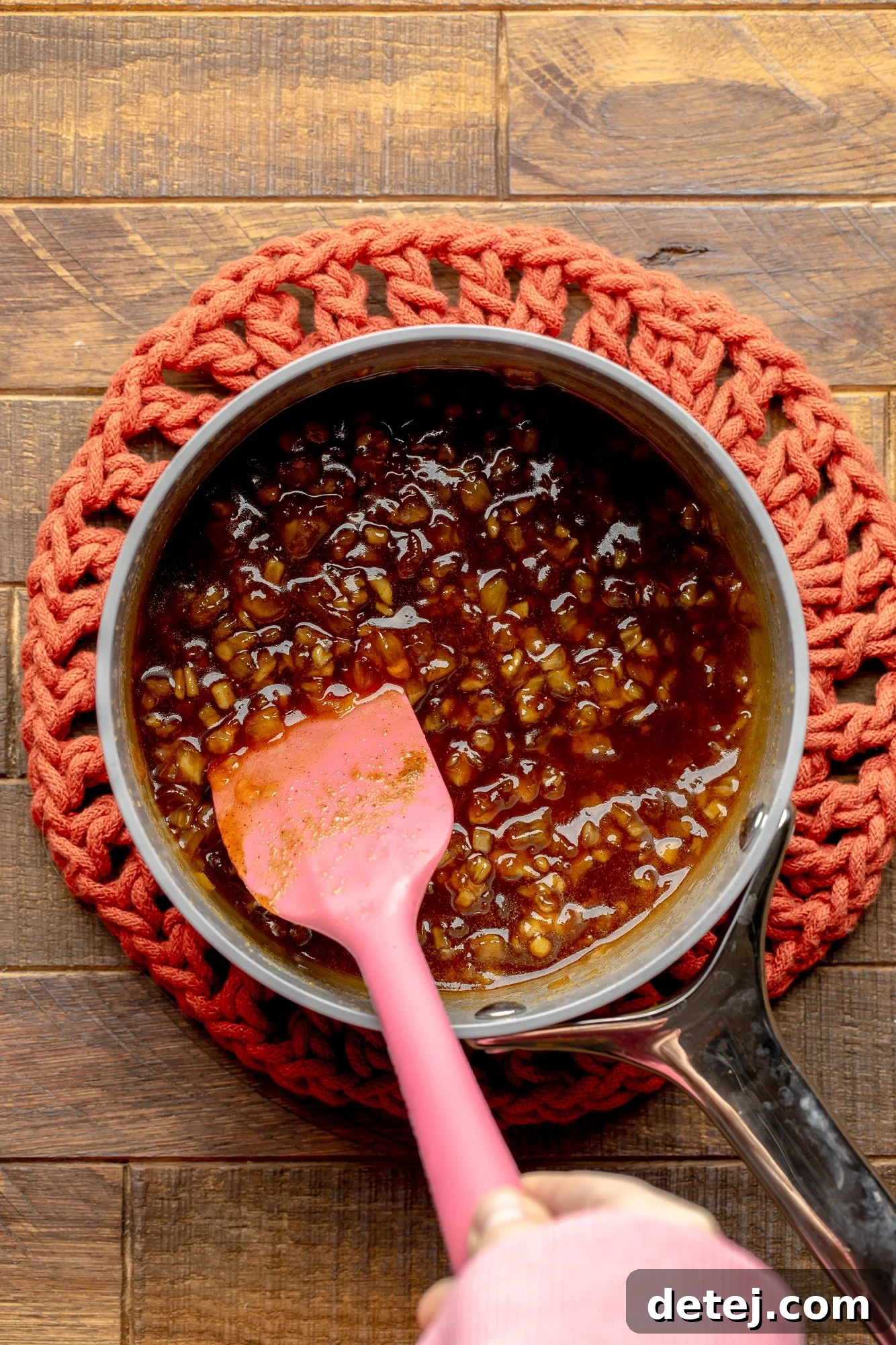 overhead view of a pink spatula stirring a pineapple glaze in a saucepan.