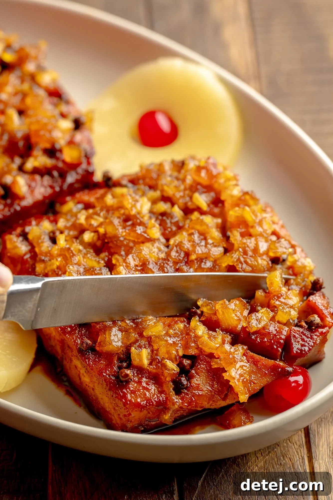 side view of a knife slicing into a pineapple glazed tofu roast in a serving dish.