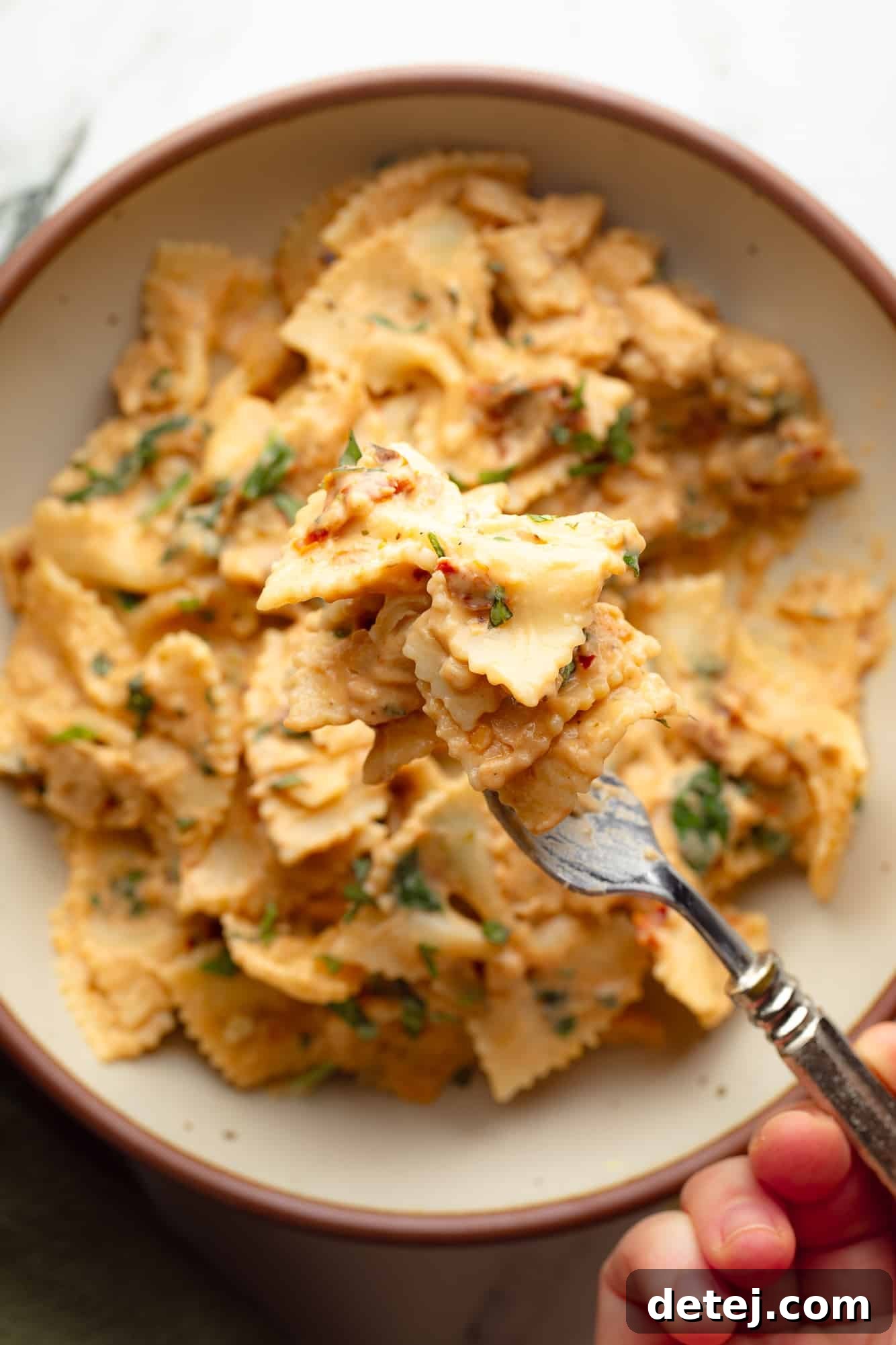 close up on a forkful of vegan marry me pasta being held above a bowl of pasta.