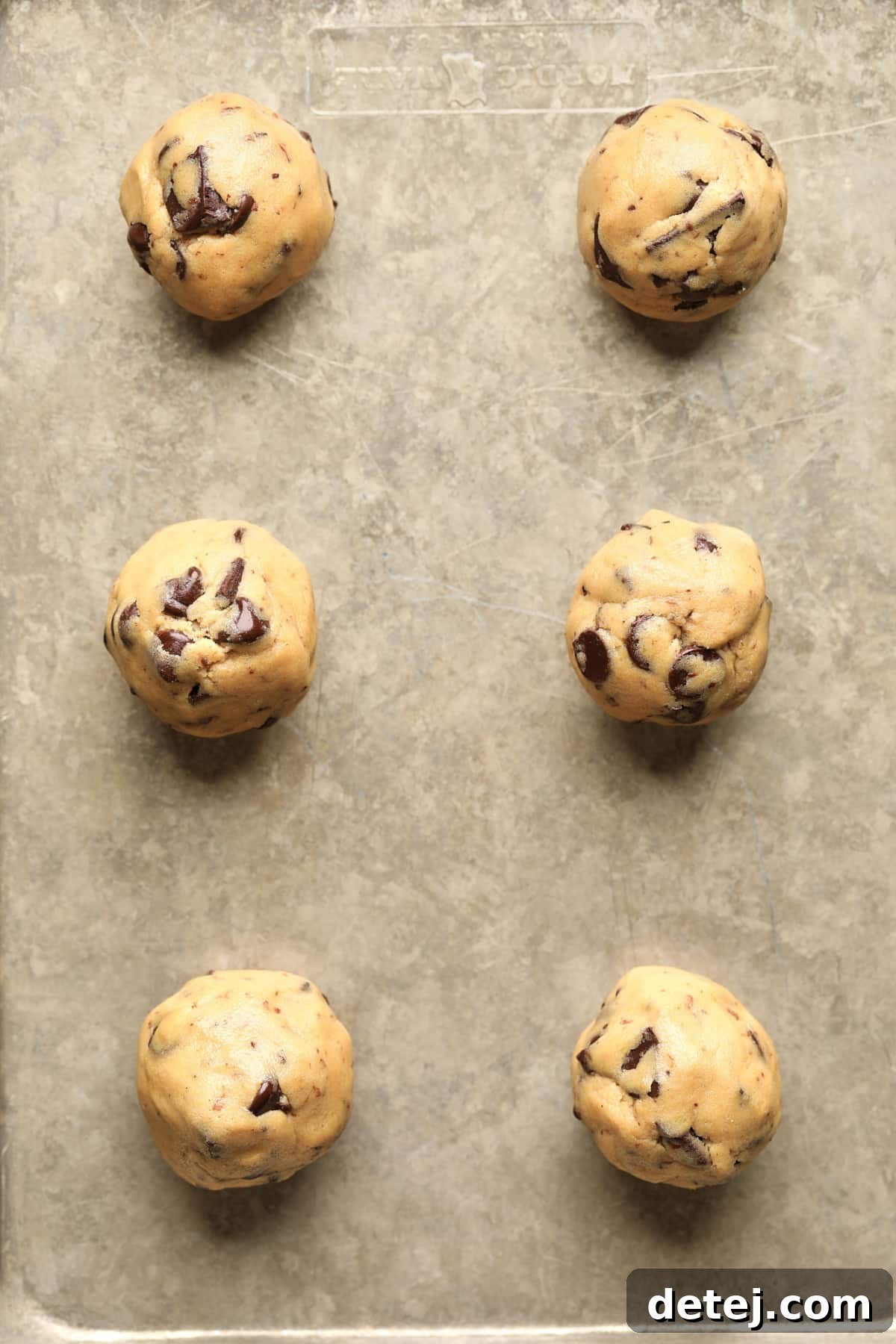 Evenly spaced balls of vegan chocolate chip cookie dough neatly arranged on a baking sheet, awaiting their turn in the oven.