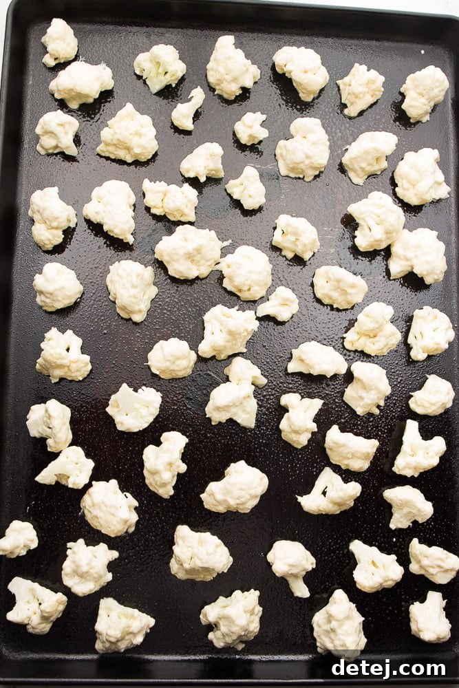 Cauliflower florets perfectly coated in a light batter, spread on a baking sheet, ready for oven roasting