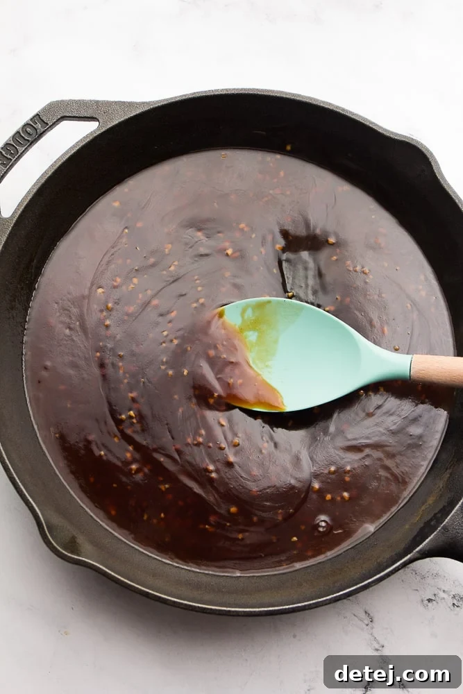 Thick and glossy sticky sesame sauce being stirred in a cast iron pan on the stovetop