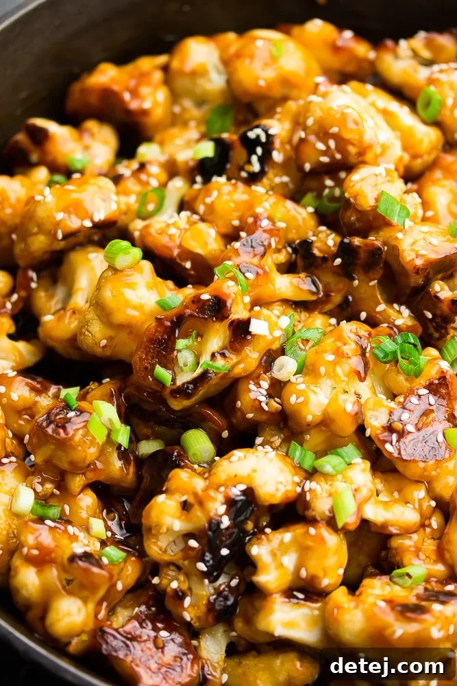 Close-up of baked sesame cauliflower in a pan, garnished with fresh chopped green onions and sesame seeds