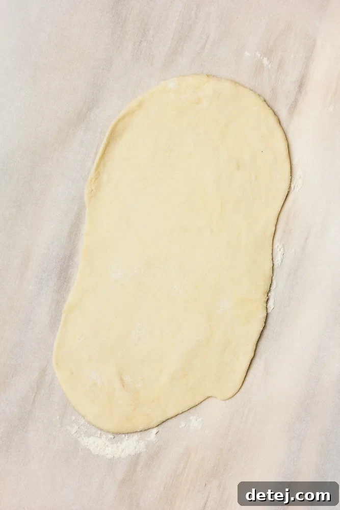 A single piece of vegan naan dough, perfectly rolled out into an oval shape, ready for cooking.