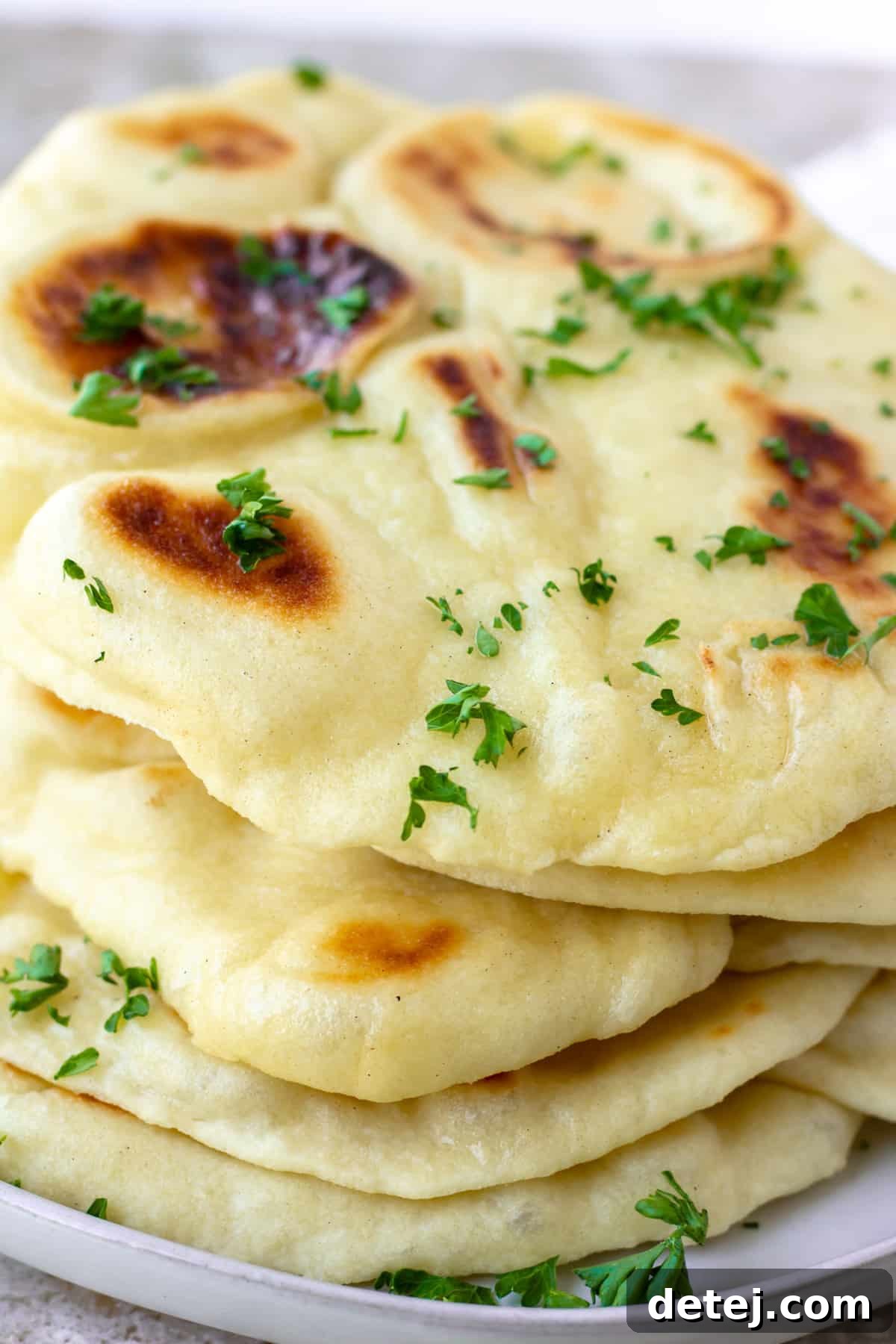 A stack of perfectly cooked vegan naan, adorned with fresh herbs, on a white plate ready to be served.