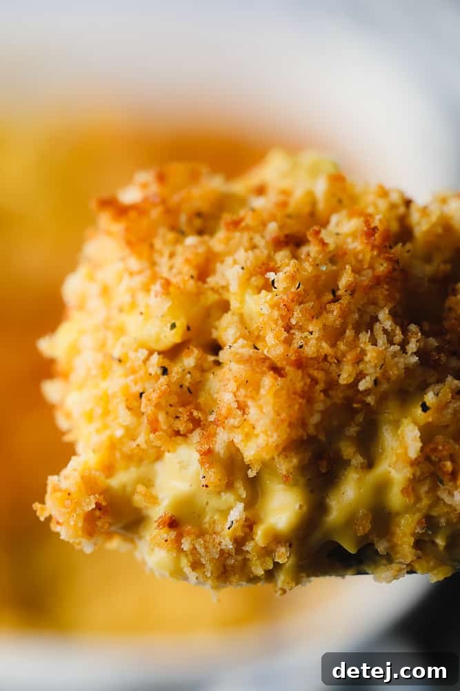 Spatula lifting a portion of golden-baked vegan mac and cheese from a pan, showcasing its rich texture and crispy topping.