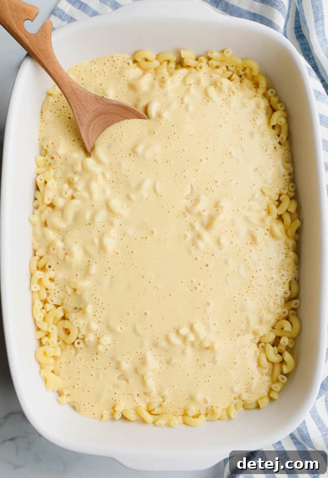 A casserole dish filled with cooked noodles generously coated in a rich, creamy vegan cheese sauce, ready for topping.