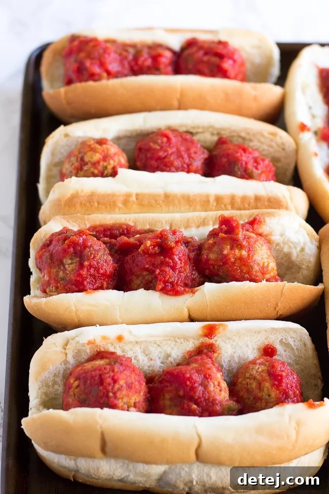 Unbaked vegan meatball subs on a baking sheet, topped with sauce, prior to adding cheese.