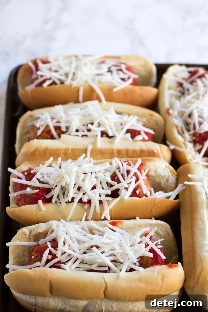 Vegan meatball subs topped with shredded non-dairy cheese, ready for baking.