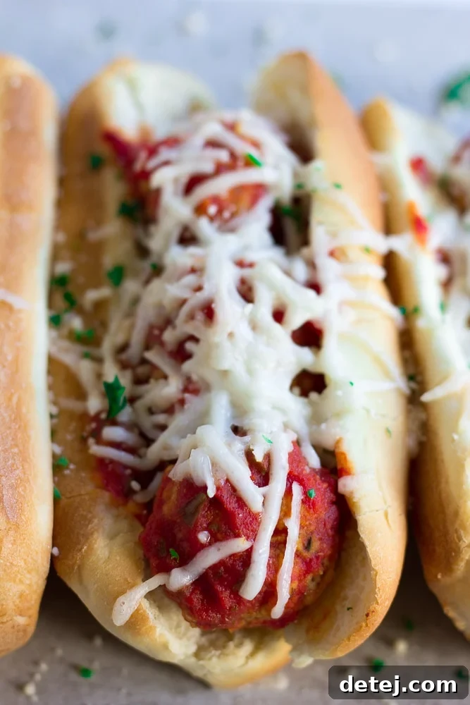Close-up of a perfectly baked vegan meatball sub, showcasing the melted cheese and a cross-section of the flavorful meatballs.