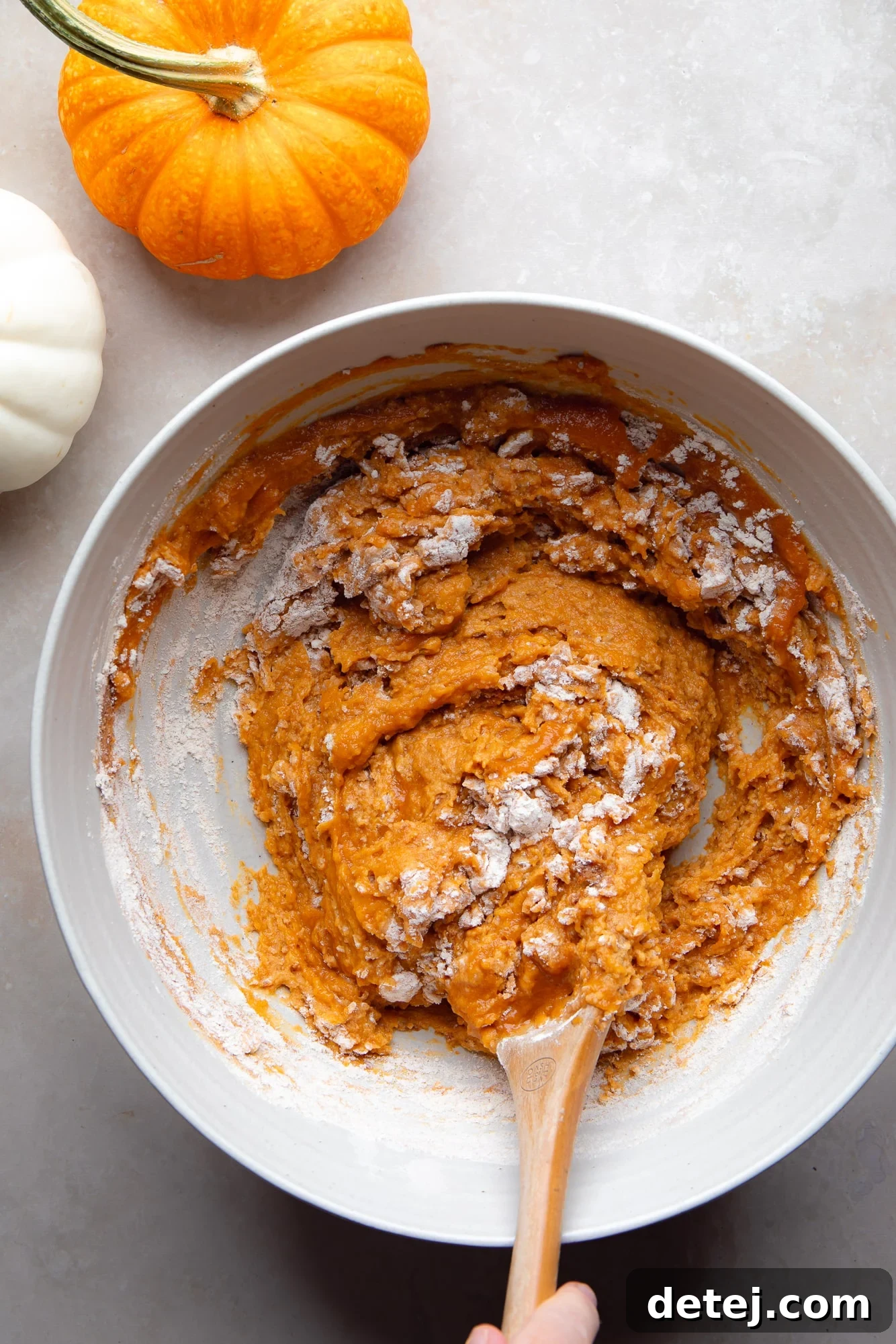 Stirring the vegan pumpkin muffin batter in a large bowl with a wooden spoon, incorporating optional mix-ins.