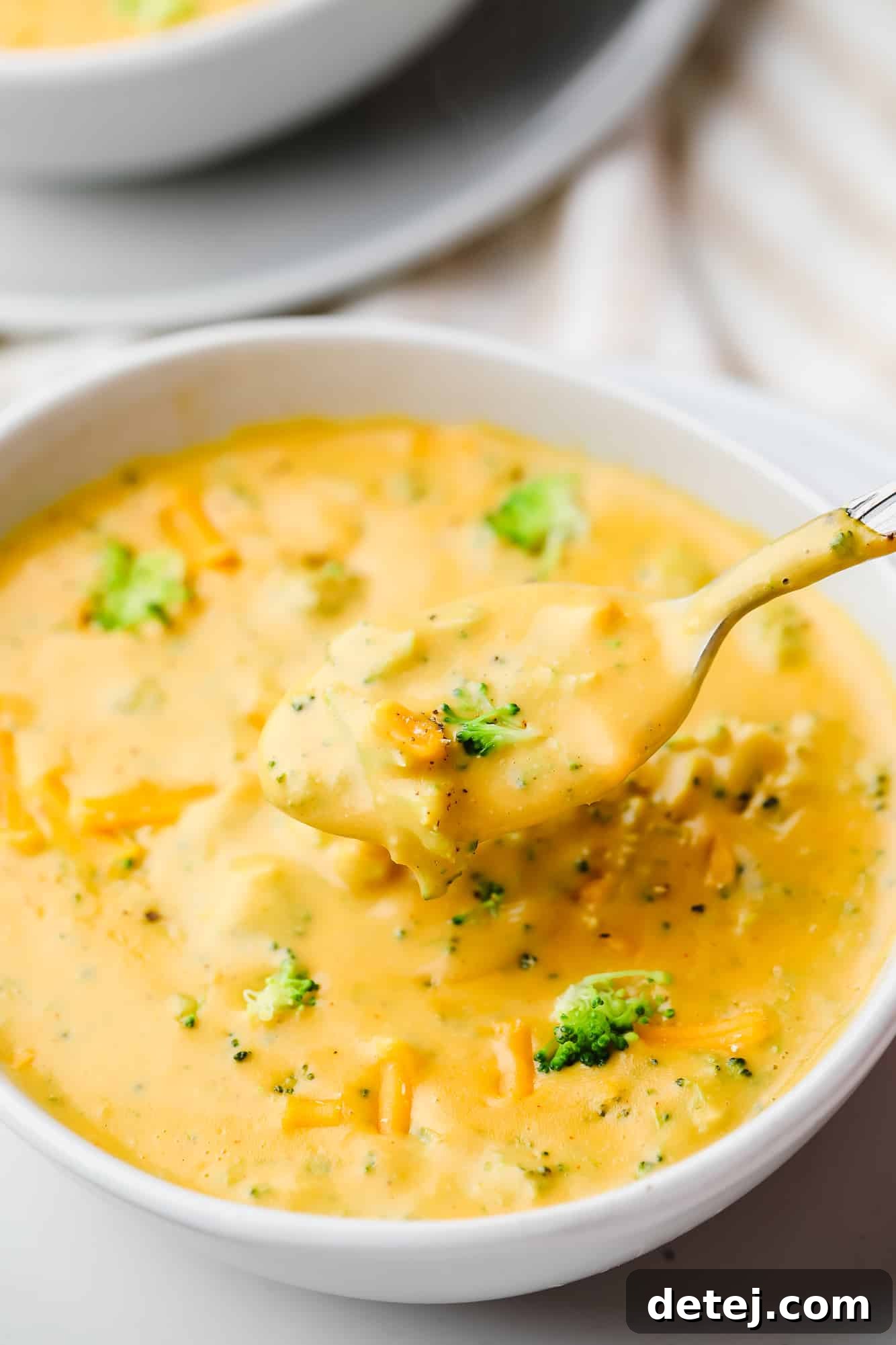 Velvety Vegan Broccoli Cheddar Soup 3 a spoon taking a scoop of broccoli cheddar soup out of a white bowl.