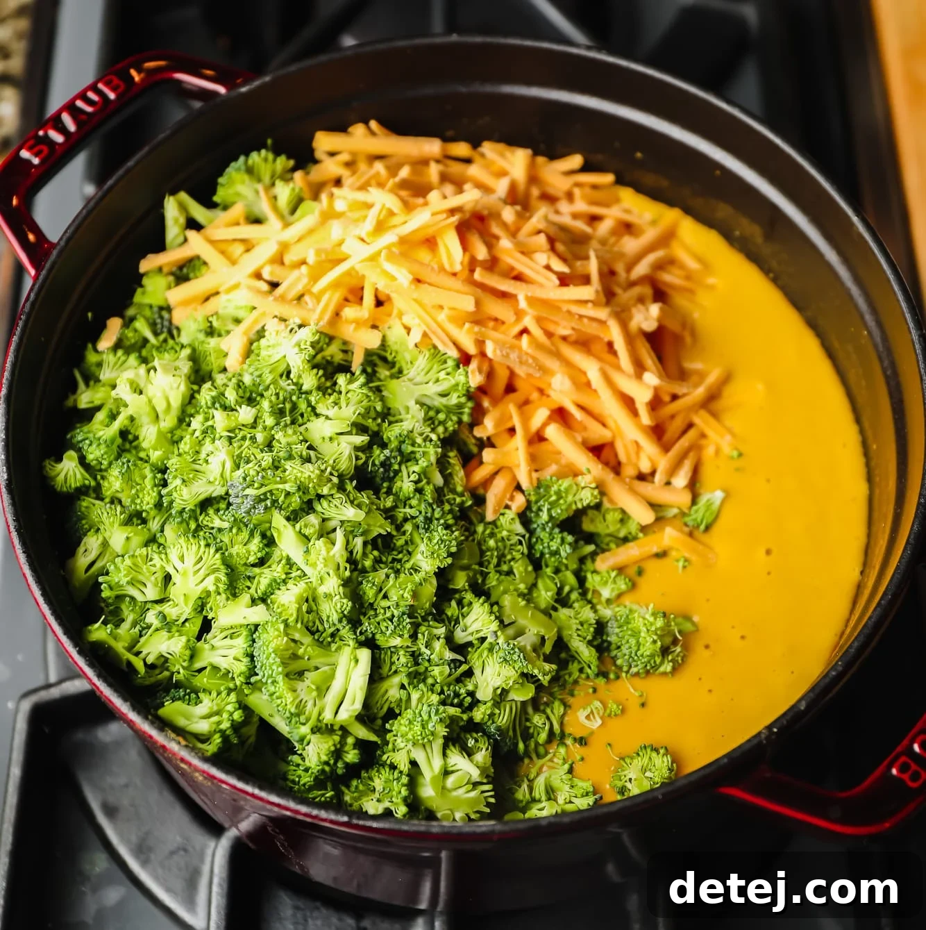 Velvety Vegan Broccoli Cheddar Soup 6 broccoli florets and shredded vegan cheese on top of a pot of broccoli cheddar soup in a large black pot.