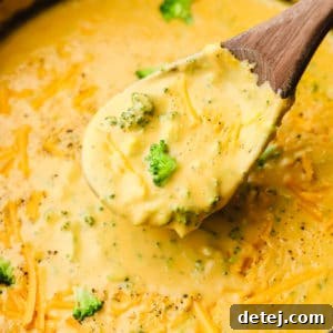 Velvety Vegan Broccoli Cheddar Soup 9 close up on a wooden spoon scooping vegan broccoli cheddar soup out of a pot.