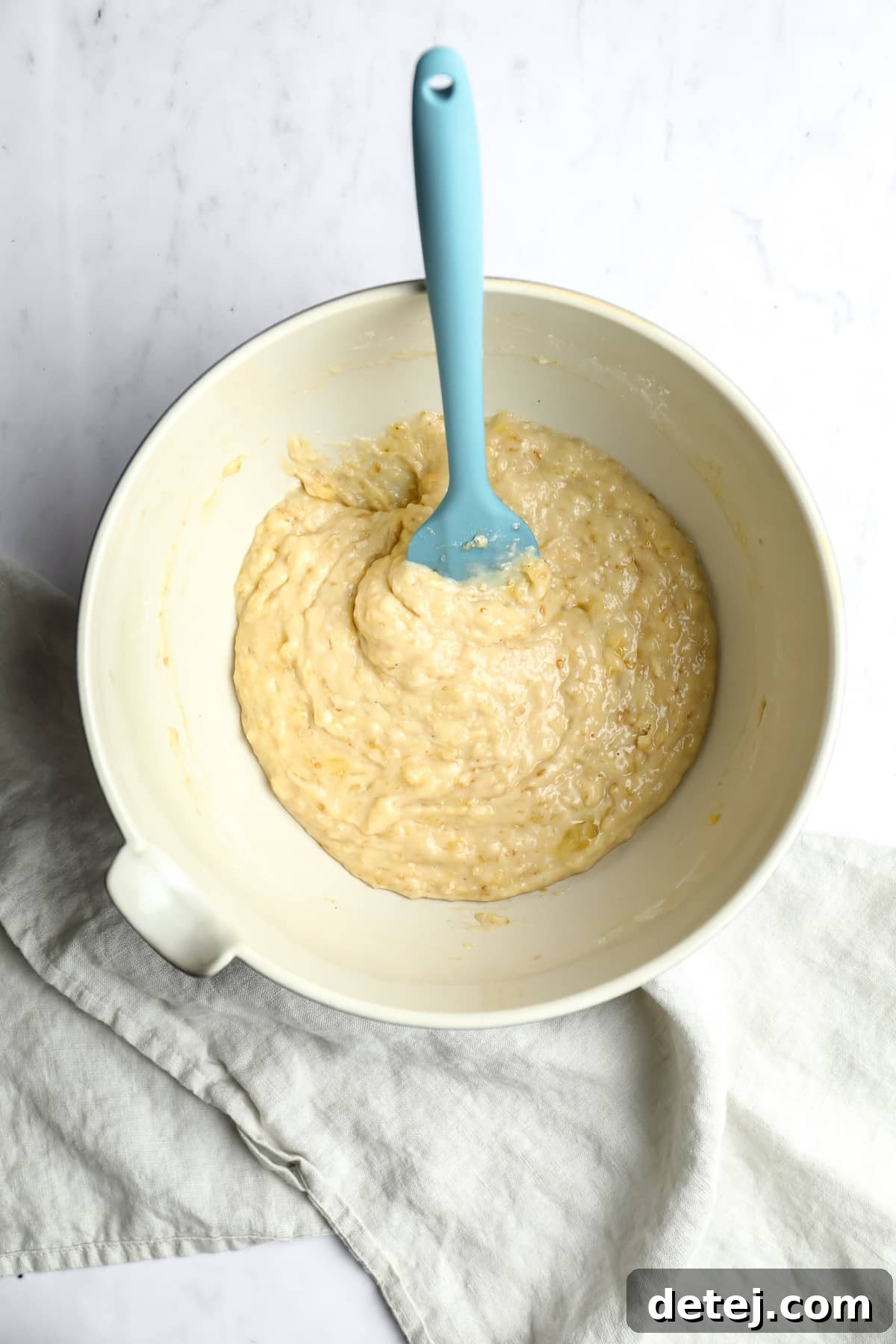 bowl of banana bread batter with blue spatula in it