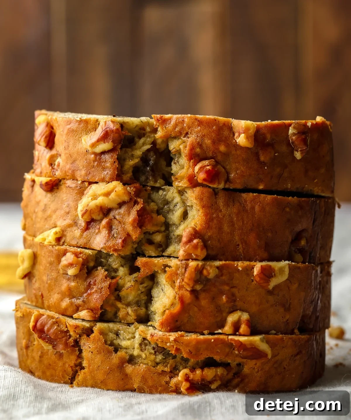 stacked sliced vegan banana bread with walnuts throughout, wood backdrop