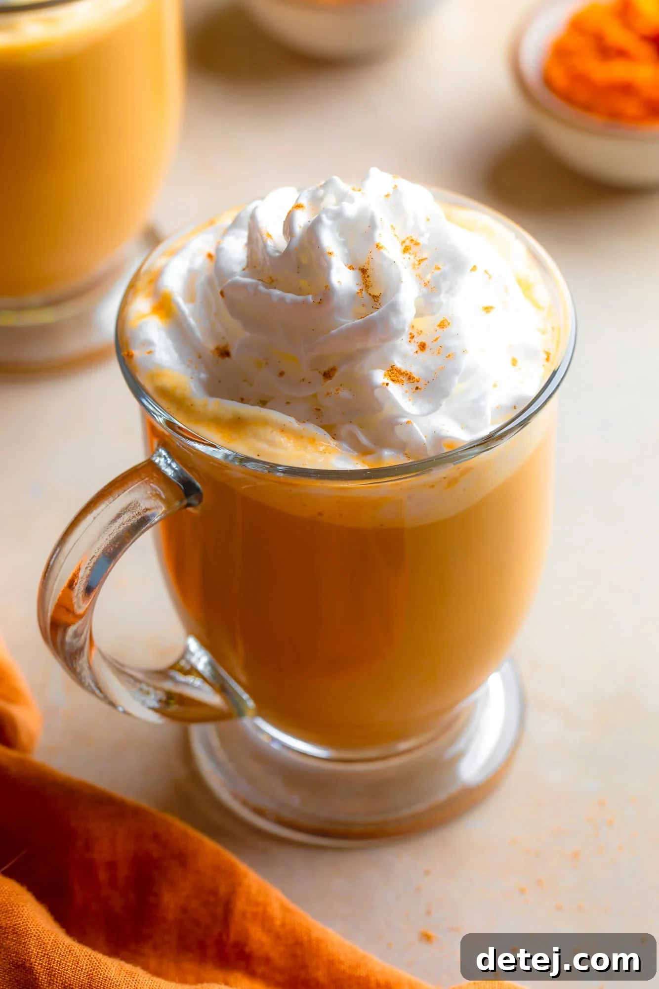 A beautifully presented glass mug filled with a creamy vegan pumpkin spice latte, topped generously with dairy-free whipped cream and a sprinkle of cinnamon, evoking a perfect autumn morning.